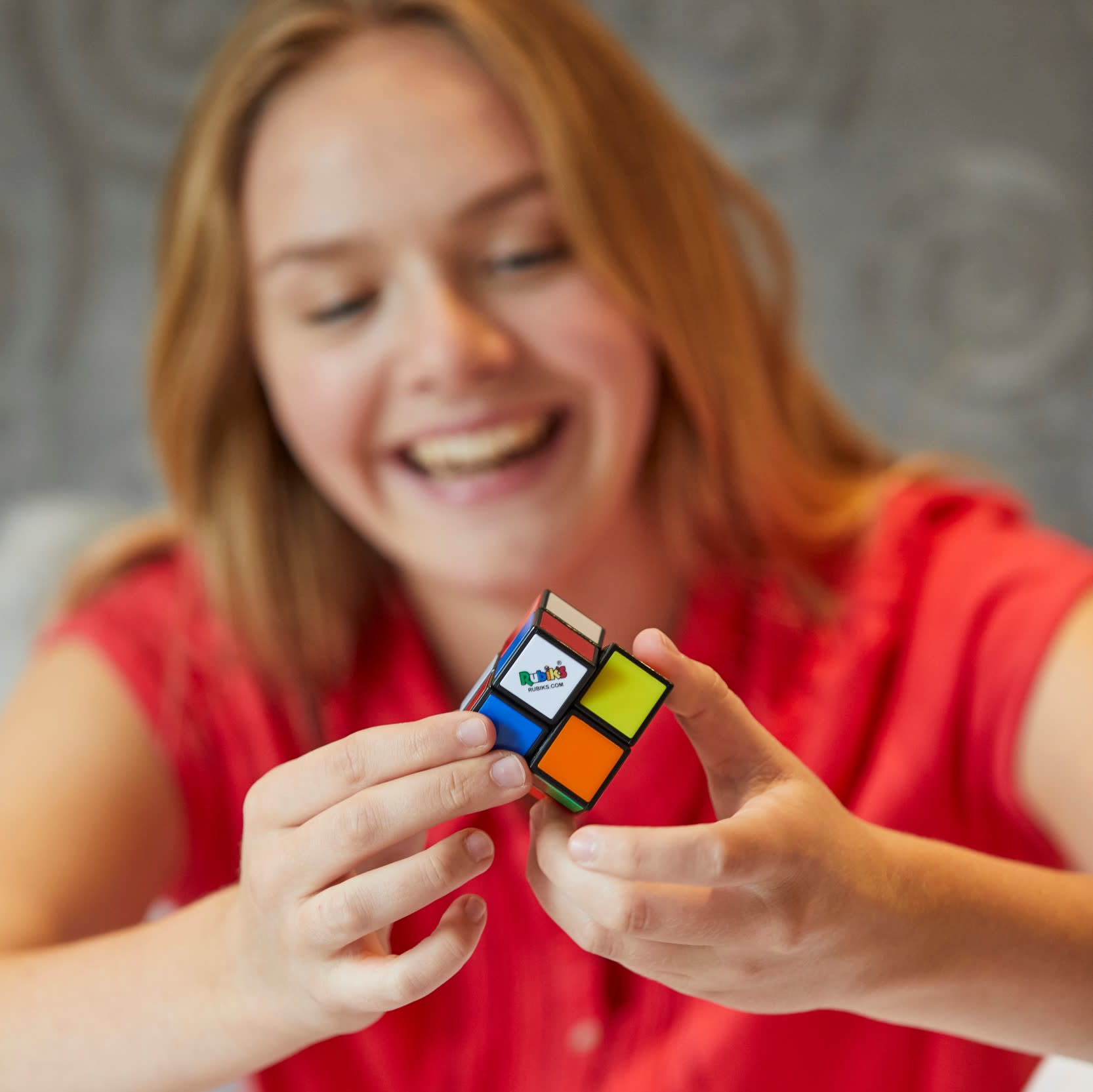 Una ragazza sorridente tiene in mano un cubo di Rubik. Il cubo è nelle sue mani e lei guarda in basso.