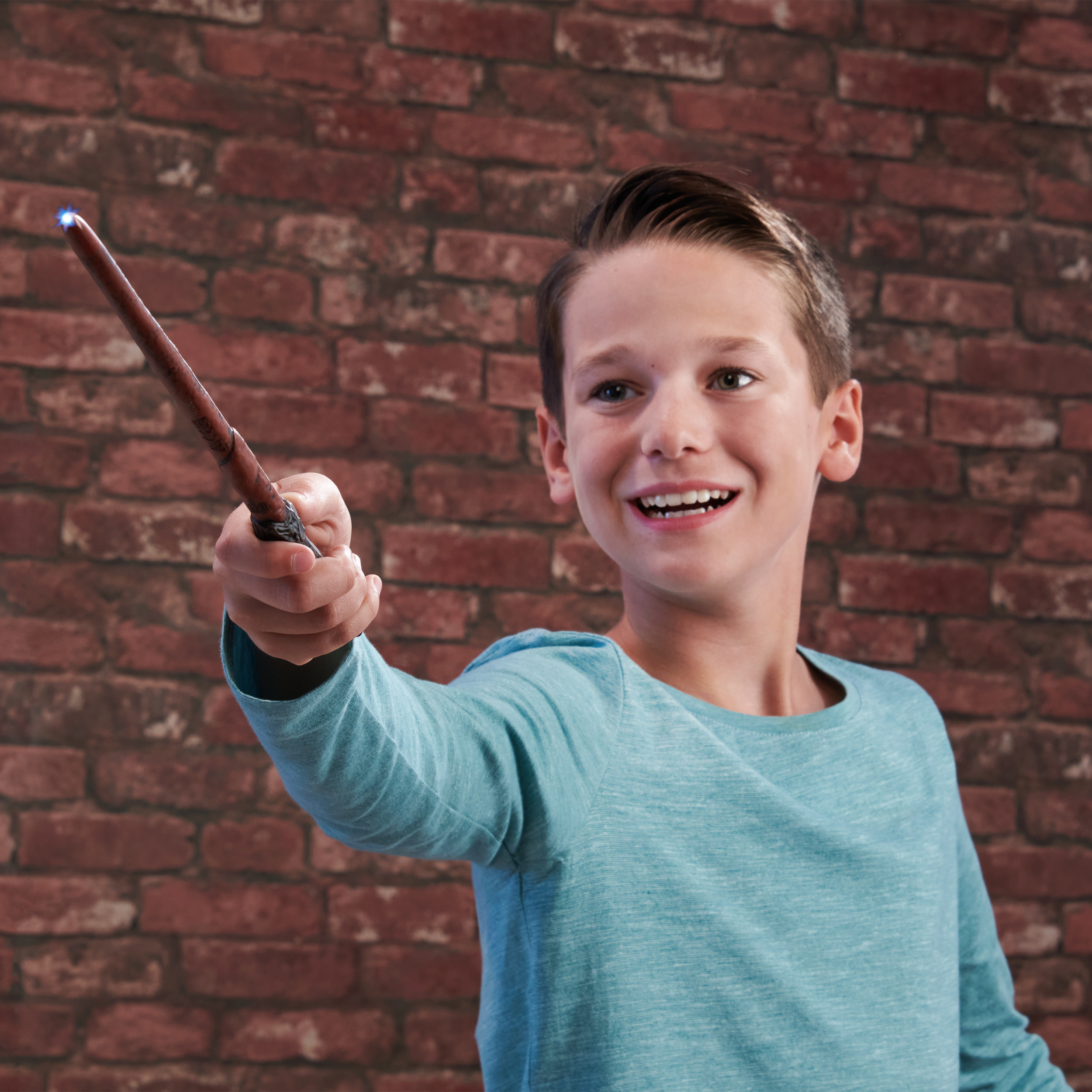 Chłopiec trzymający różdżkę, uśmiechnięty, z ceglanym tłem. Różdżka jest podświetlona.