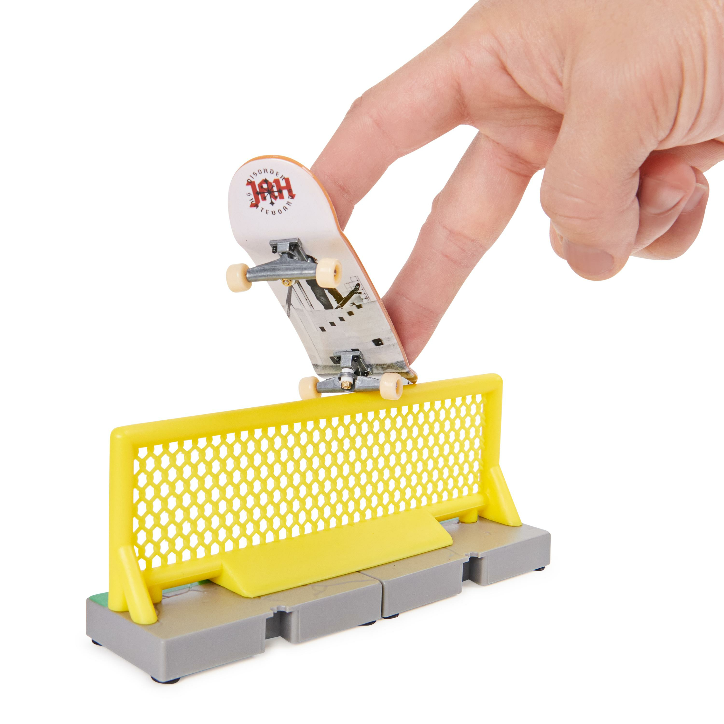 Hand hält ein Miniatur-Skateboard über einer gelb-grauen Rampe. Weißer Hintergrund.