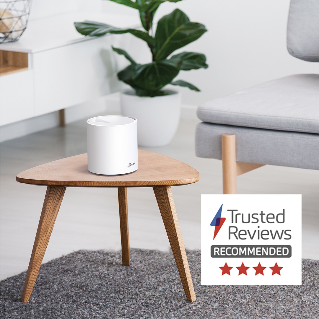 Weißer Router auf einem Holztisch. Grauer Teppich und moderne Möbel. Weißer Hintergrund. "Trusted Reviews"-Logo.