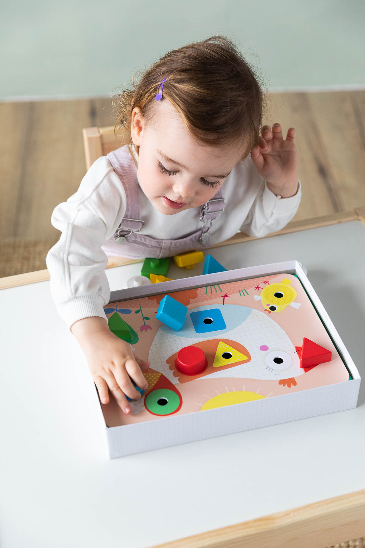 Una bambina gioca con un puzzle in legno. Il puzzle ha la forma di un uccello e forme geometriche colorate.