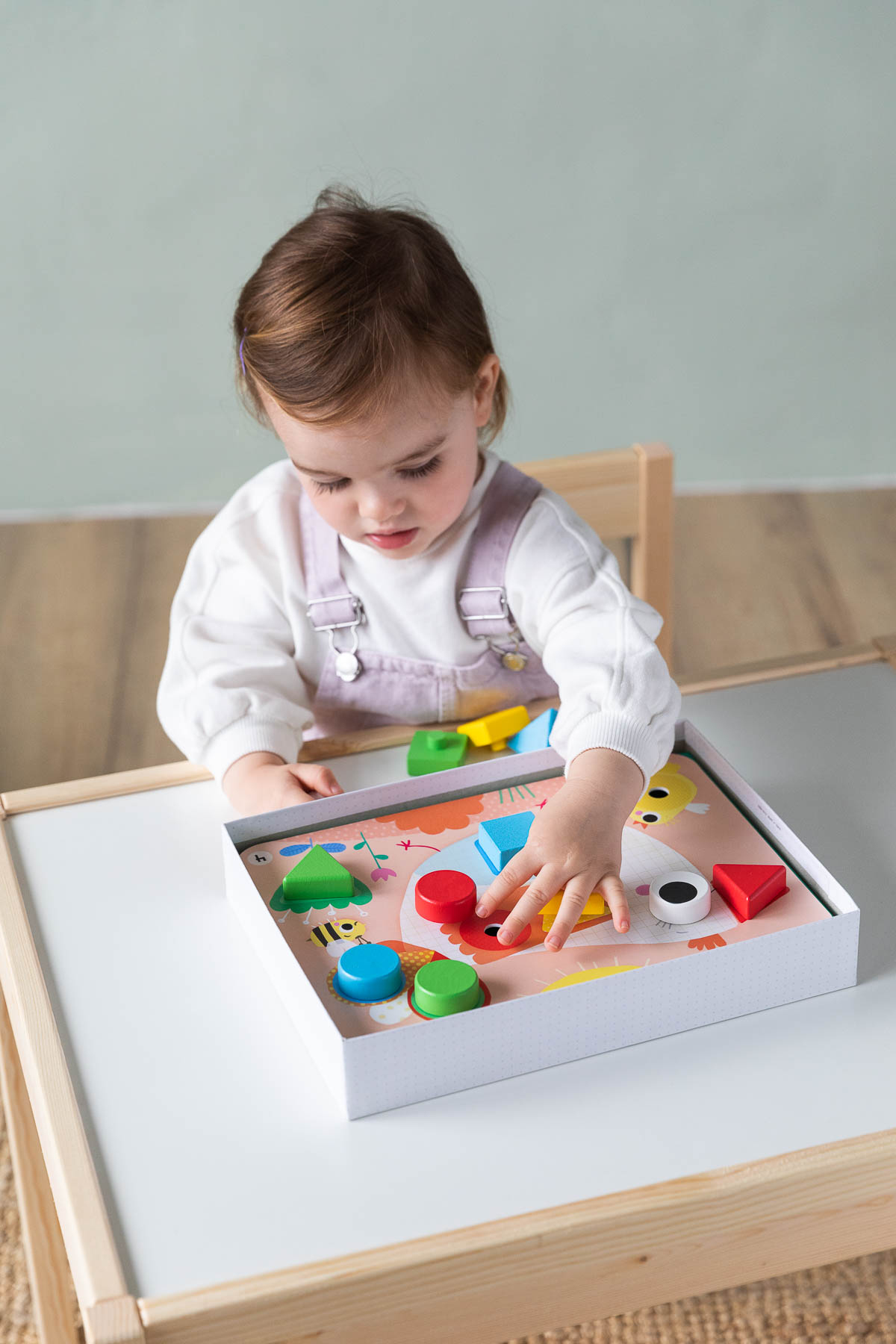 Un bambino gioca con un puzzle di legno. Forme colorate e un tavolo bianco.