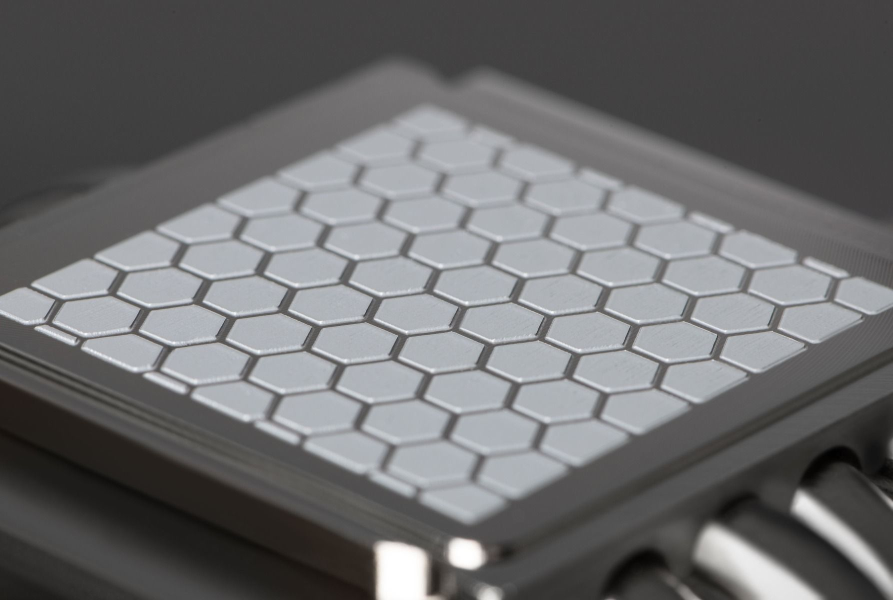 Zbliżenie srebrnego kwadratu z wzorem plastra miodu na ciemnej powierzchni.