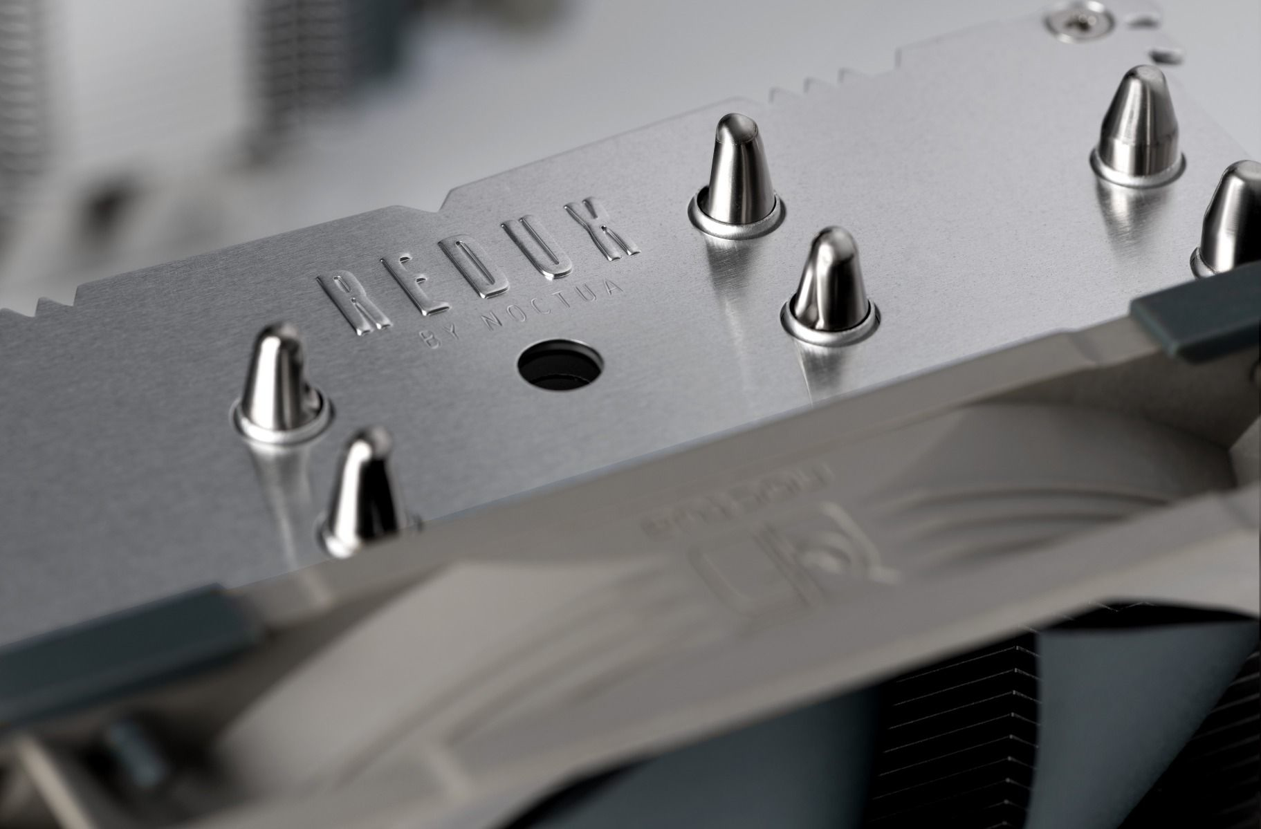 Zbliżenie chłodnicy komputera. Tekst: REDUX by Noctua. Srebrny metal z żebrami chłodzącymi.