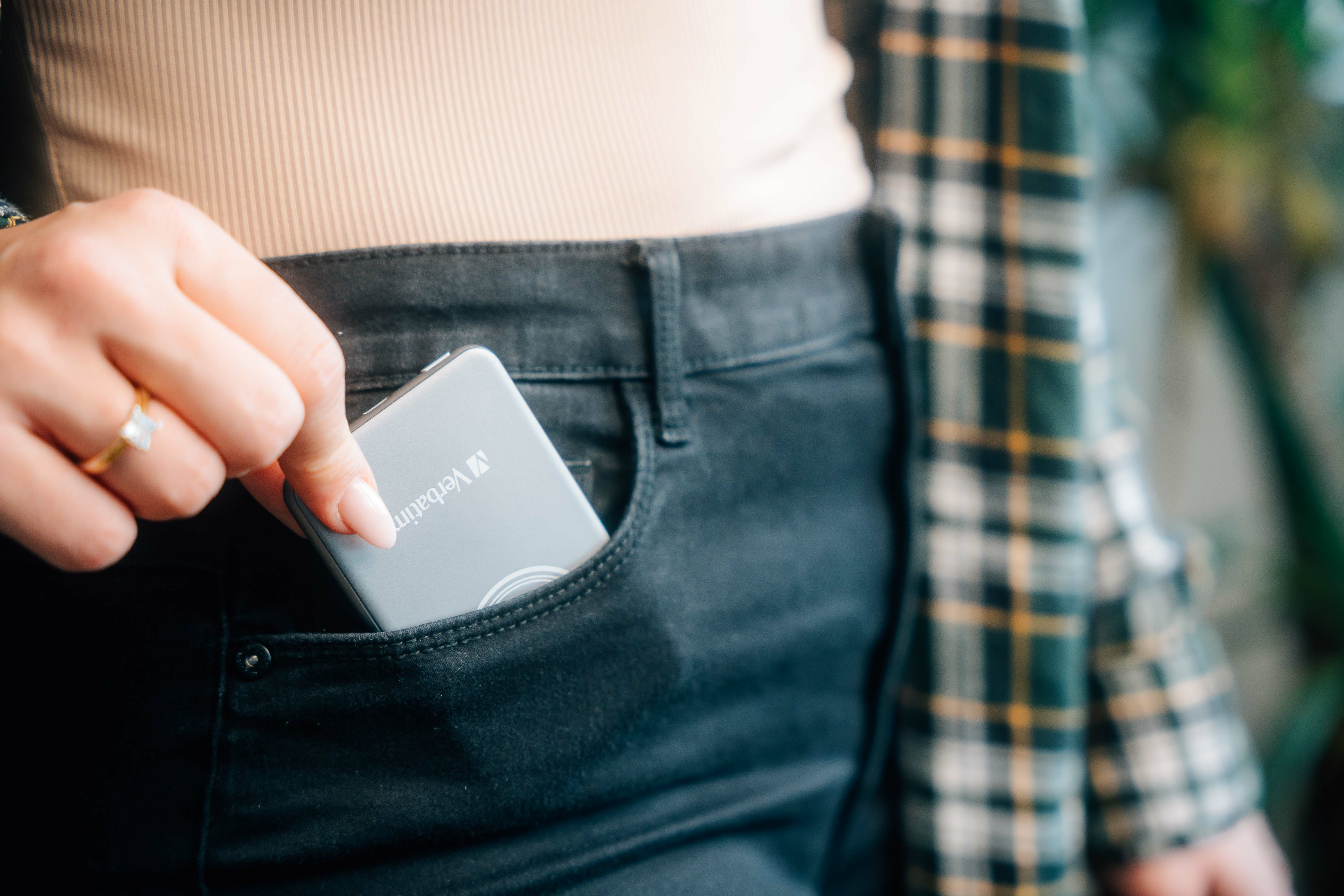 Hand van een vrouw die een zilverkleurig apparaat in een zwarte jeanszak steekt.