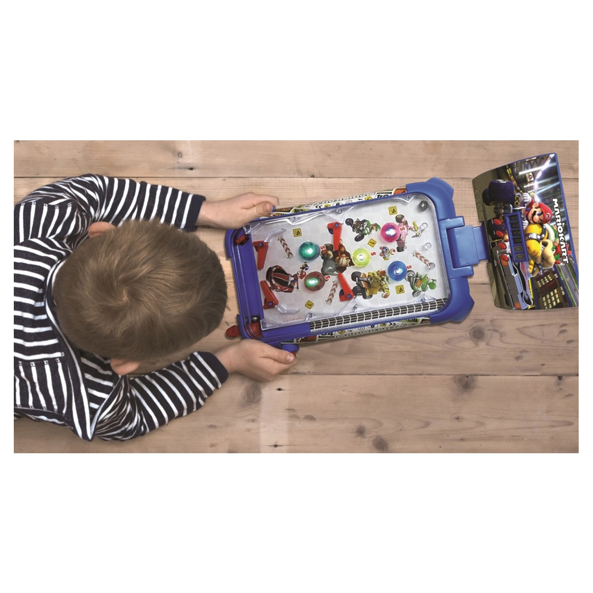 Niño jugando a un pinball de Mario Kart sobre una superficie de madera, vista cenital.