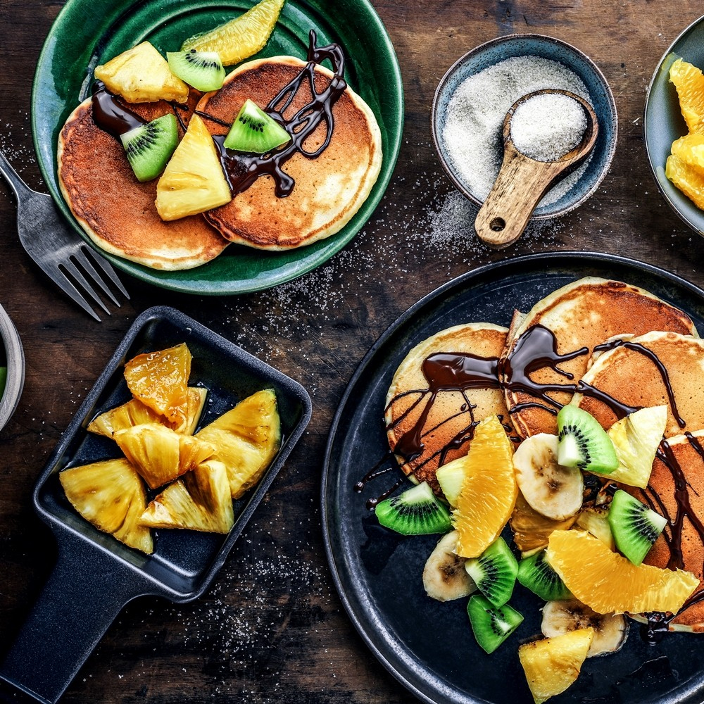 Naleśniki z owocami i sosem czekoladowym, ułożone na talerzach. Widoczne różne składniki.