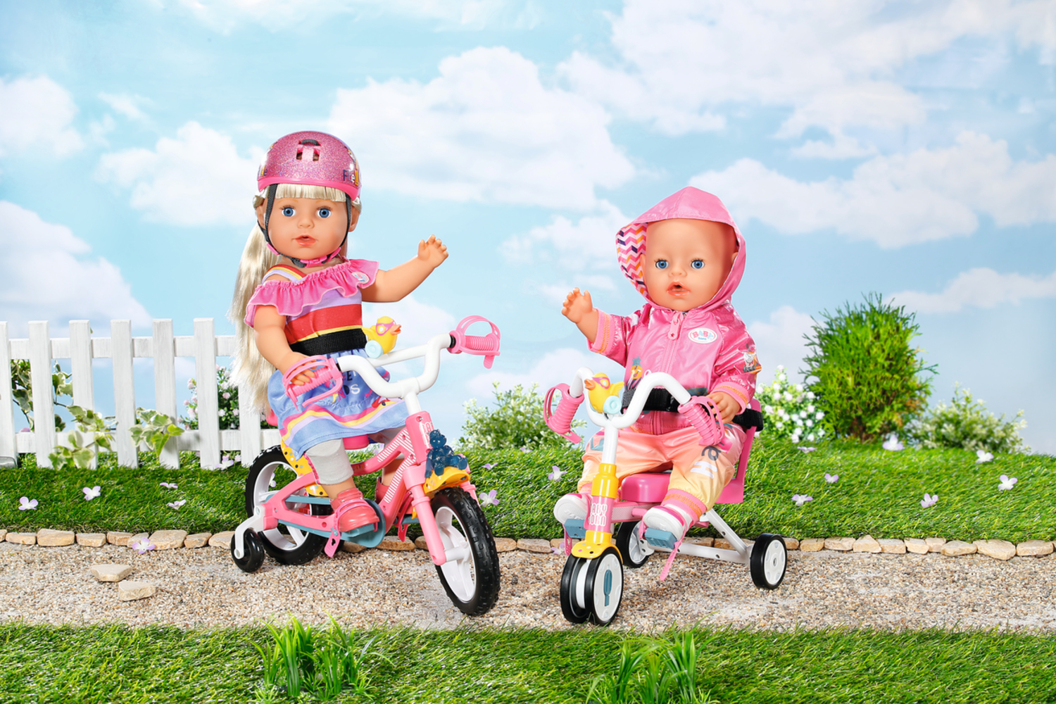 Due bambole su tricicli rosa, una con un casco, in un ambiente soleggiato e fiorito.
