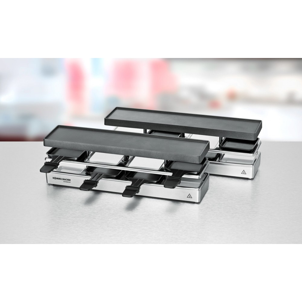 Dwa grille do raclette na białej powierzchni. Są srebrne z czarnymi płytami grillowymi i uchwytami.