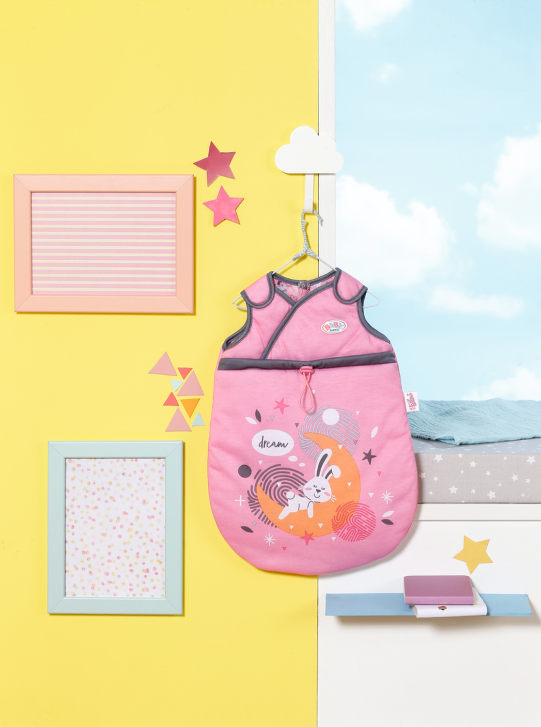Saco de dormir rosa para bebé colgado en la pared, fondo amarillo. Marcos y estrellas alrededor. Ventana.