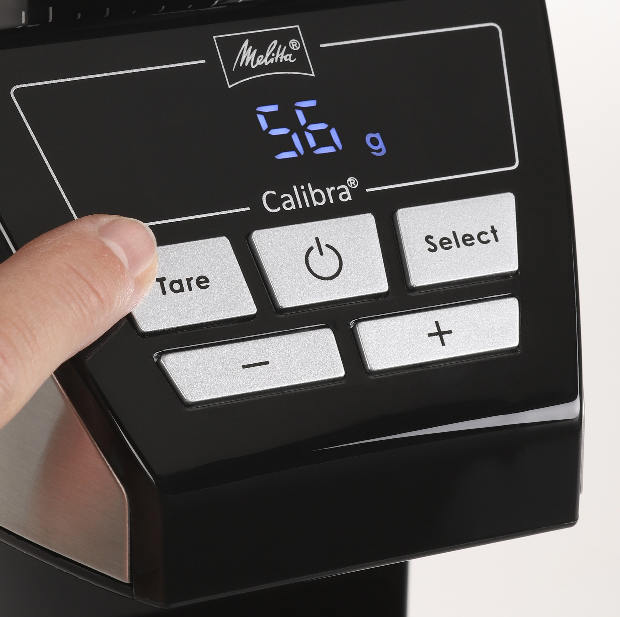 Nahaufnahme einer schwarzen Kaffeewaage mit digitaler Anzeige von 56g. Ein Finger drückt eine Taste.