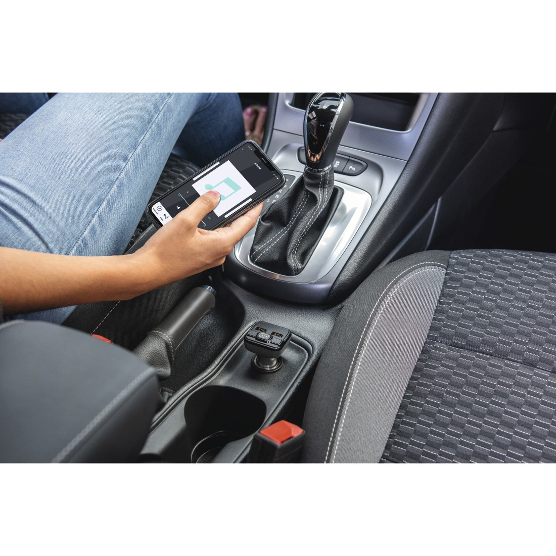Die Hand einer Person hält ein Telefon im Auto. Der Schalthebel ist sichtbar.