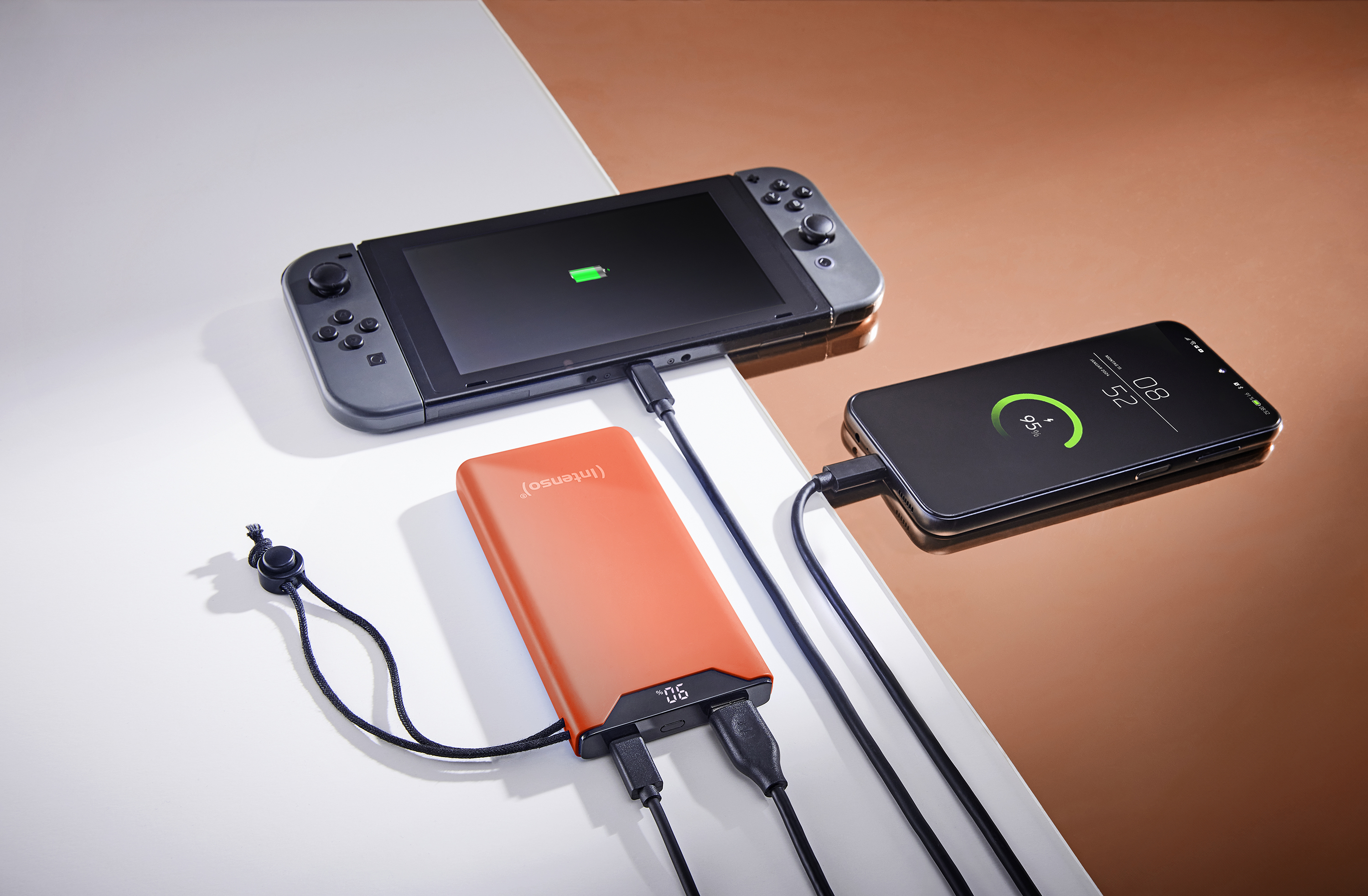 Une Nintendo Switch et un téléphone en charge. Une batterie externe orange est également visible.