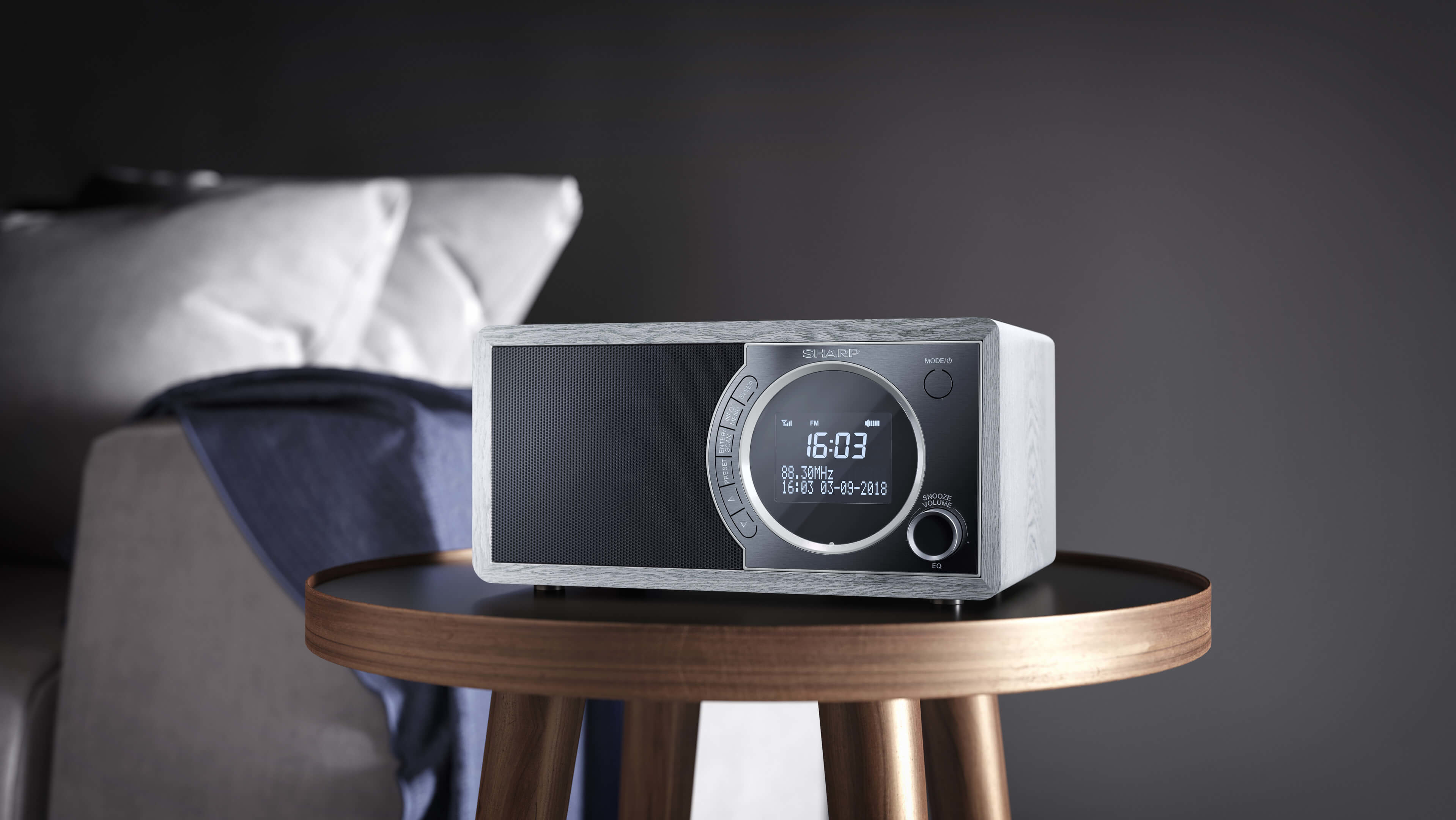 A wooden radio with a digital display and a knob, placed on a small, dark wooden table.