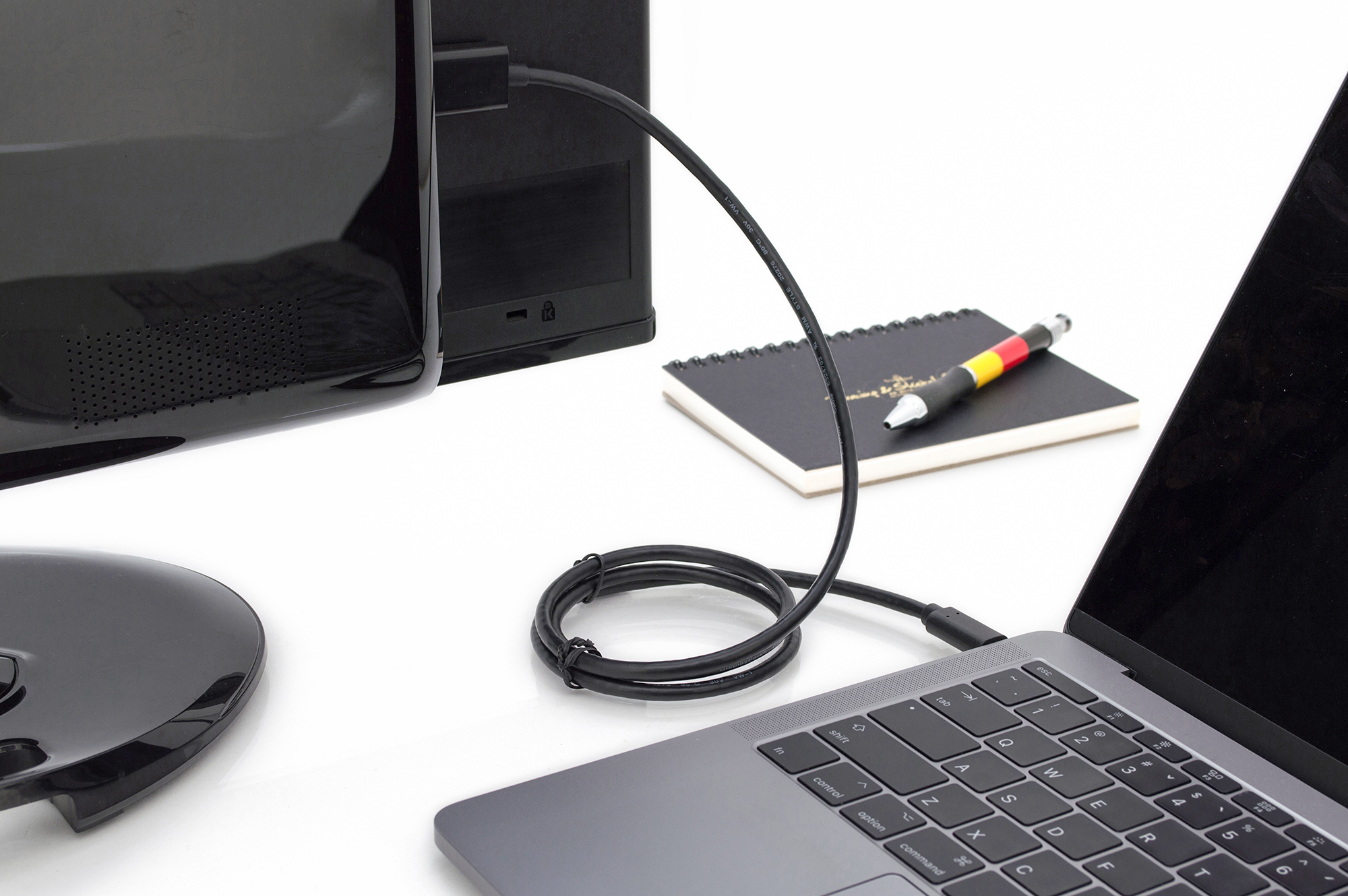 Laptop mit Monitor über ein schwarzes Kabel verbunden. Notizbuch und Stift auf dem Tisch.