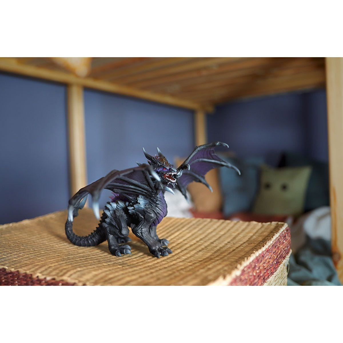 Un drago giocattolo su un tavolo. Lo sfondo è una camera da letto con un letto.