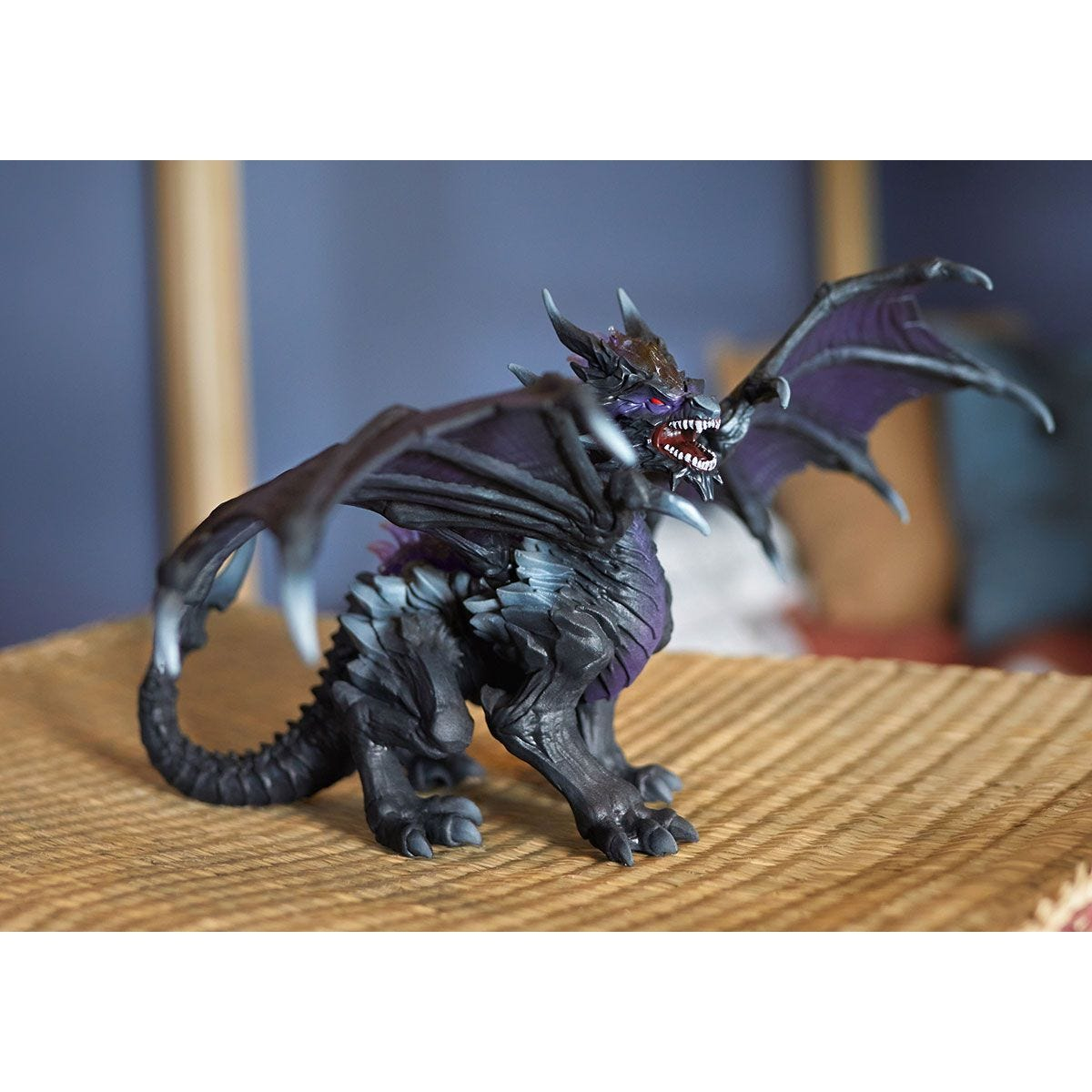 Un giocattolo a forma di drago fantasy, nero, viola e grigio, è su una superficie tessuta.