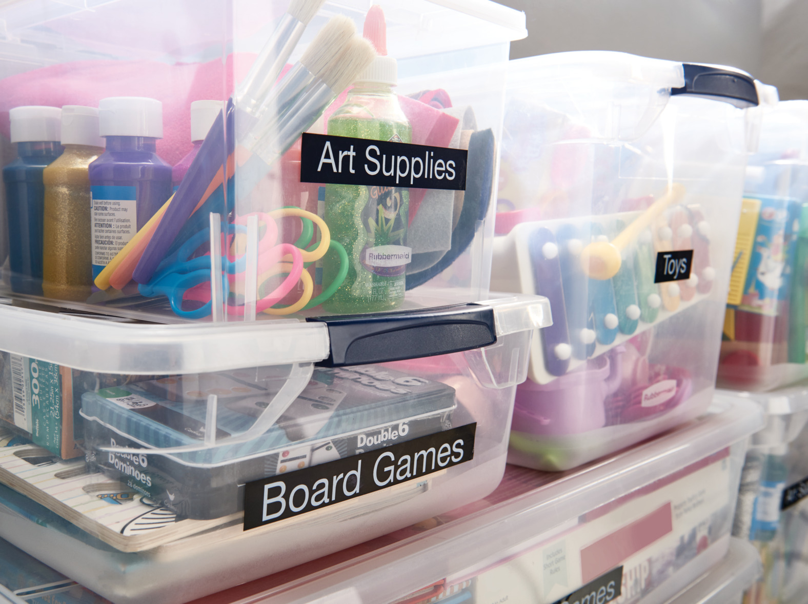 Transparente Kunststoff-Aufbewahrungsboxen mit den Aufschriften 'Art Supplies', 'Toys' und 'Board Games'.