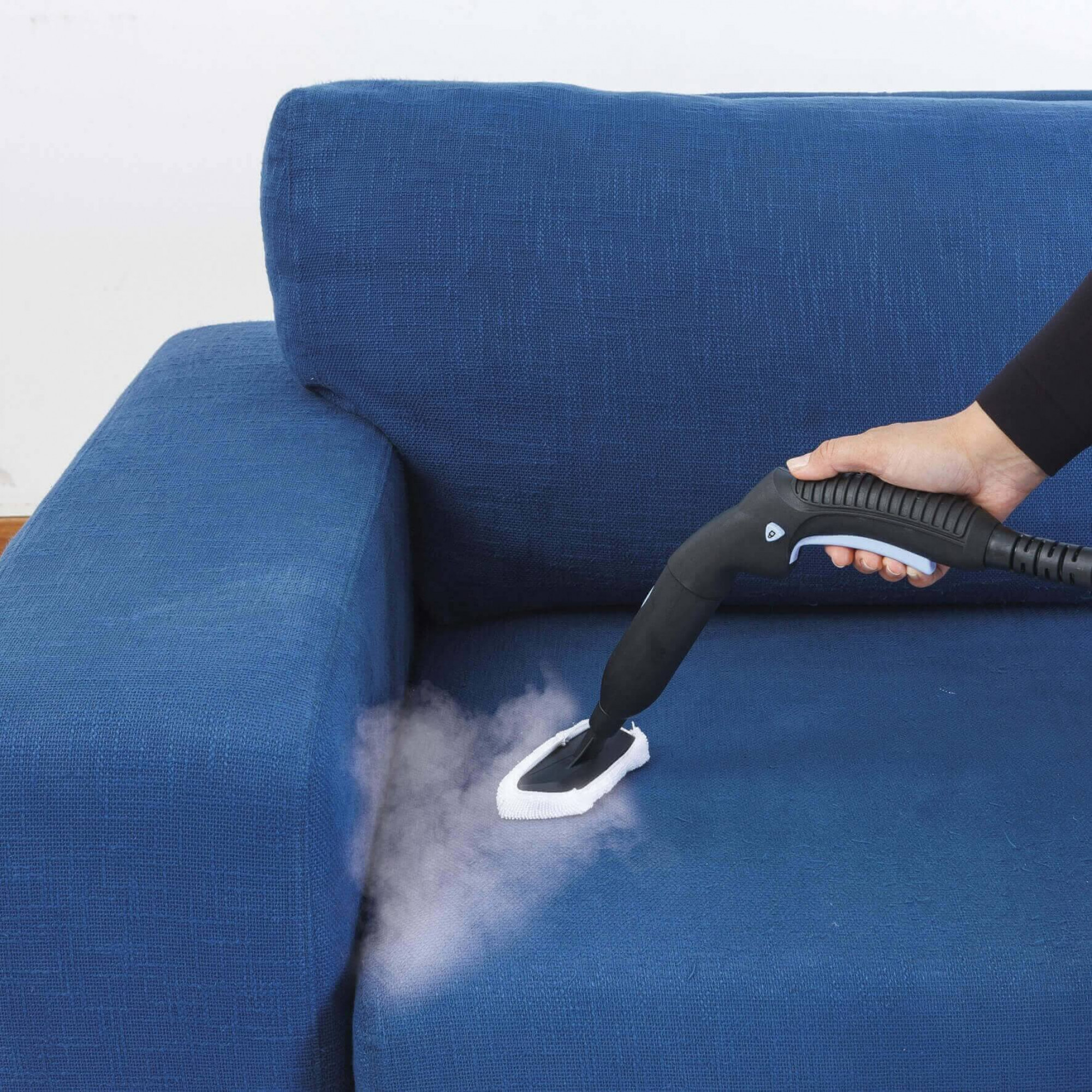 Eine Person reinigt ein blaues Sofa mit einem schwarzen Dampfreiniger.