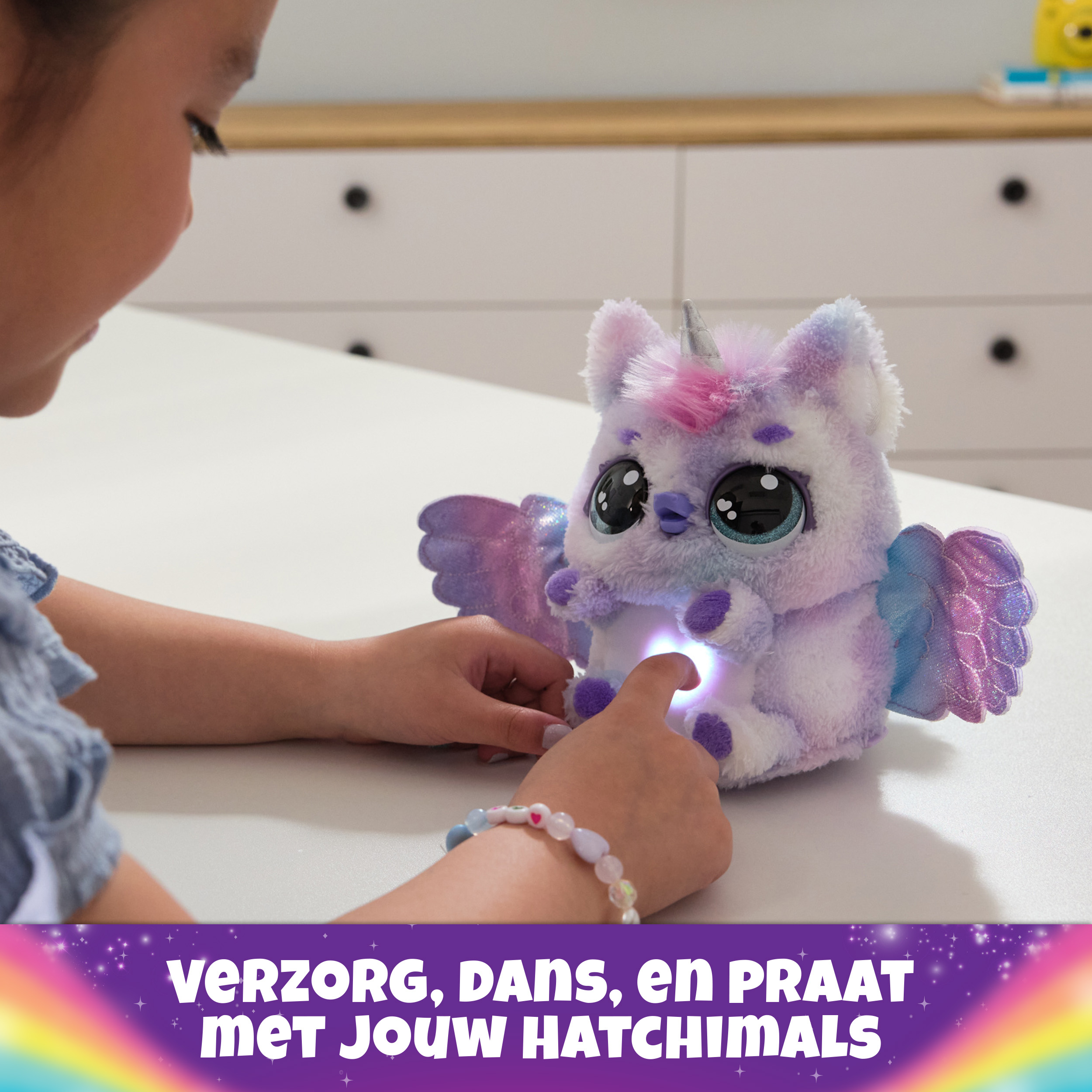 Una niña toca un juguete Hatchimals que se ilumina. Texto: Cuida, baila y habla con tus Hatchimals.