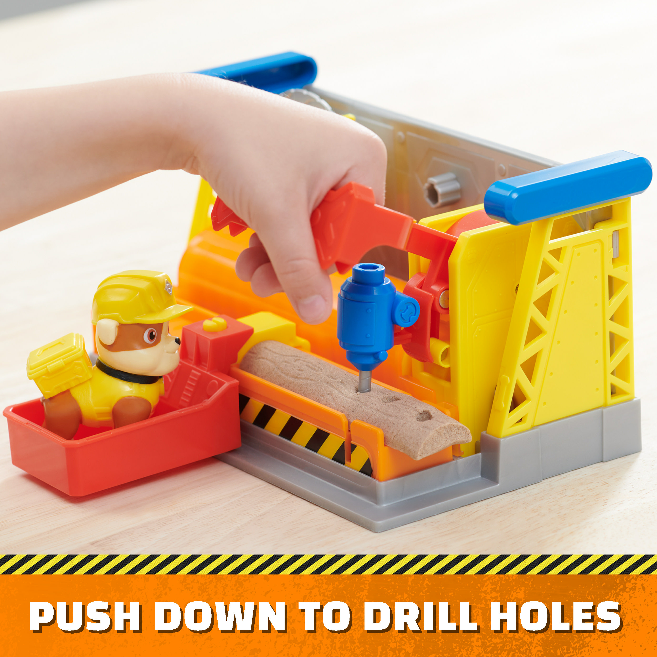 Kind benutzt Spielzeugbohrer. Spielzeughund im roten Wagen. Gelbe und orange Baustelle.