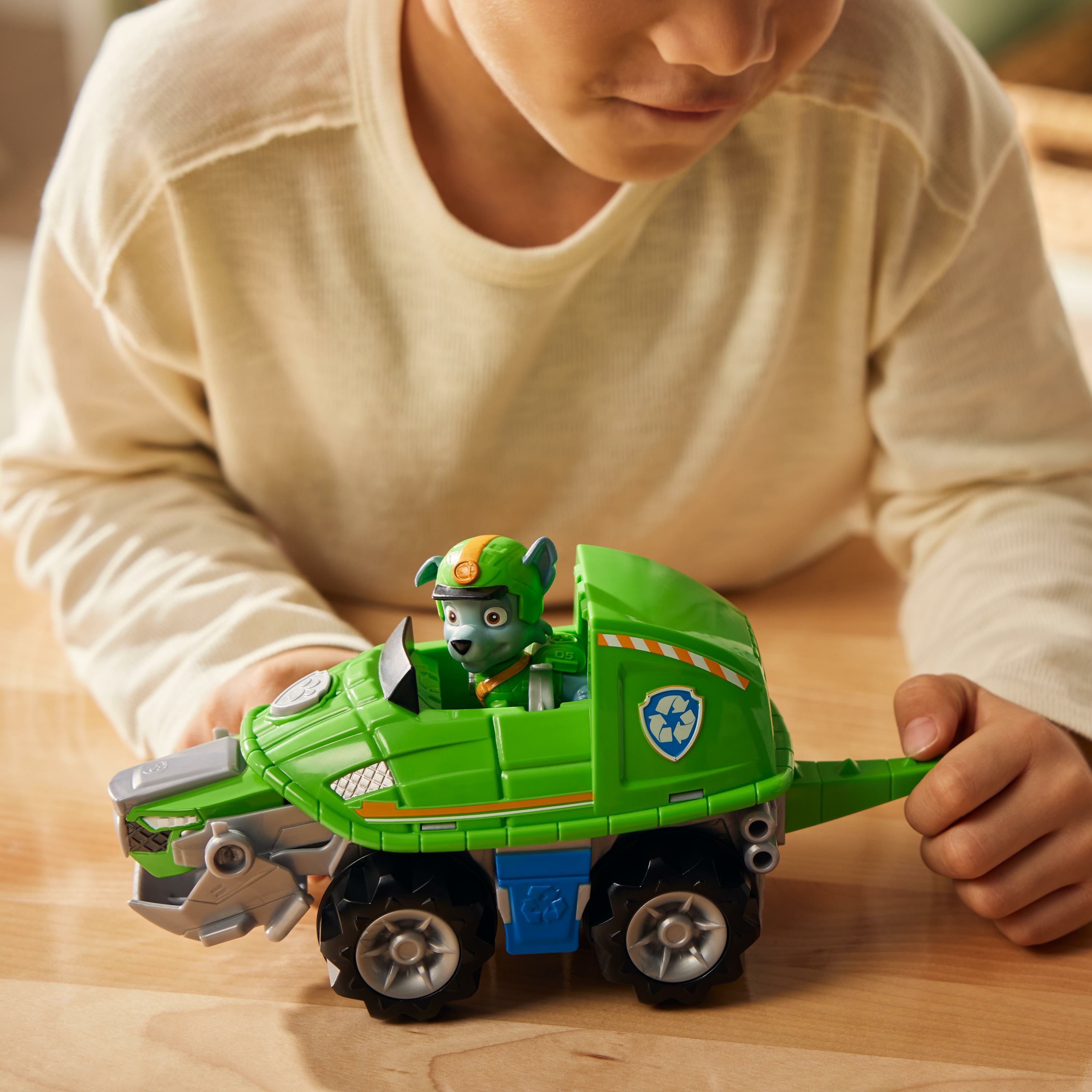 Ein Kind spielt mit einem grünen Spielzeugauto mit einer Paw Patrol-Figur darin.