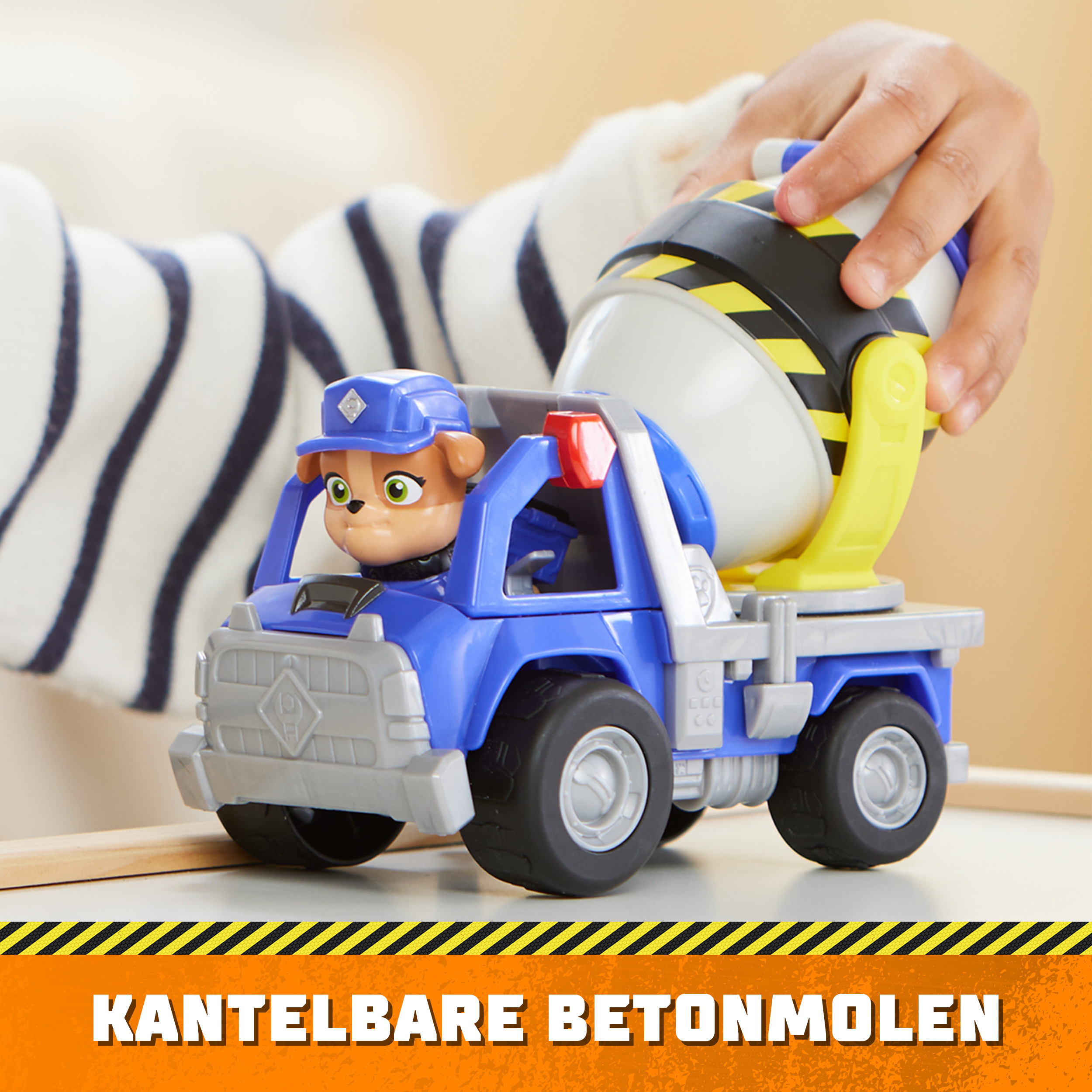 Blau-weißer Spielzeug-Zementmischwagen mit Kinderhand, auf weißem Tisch.