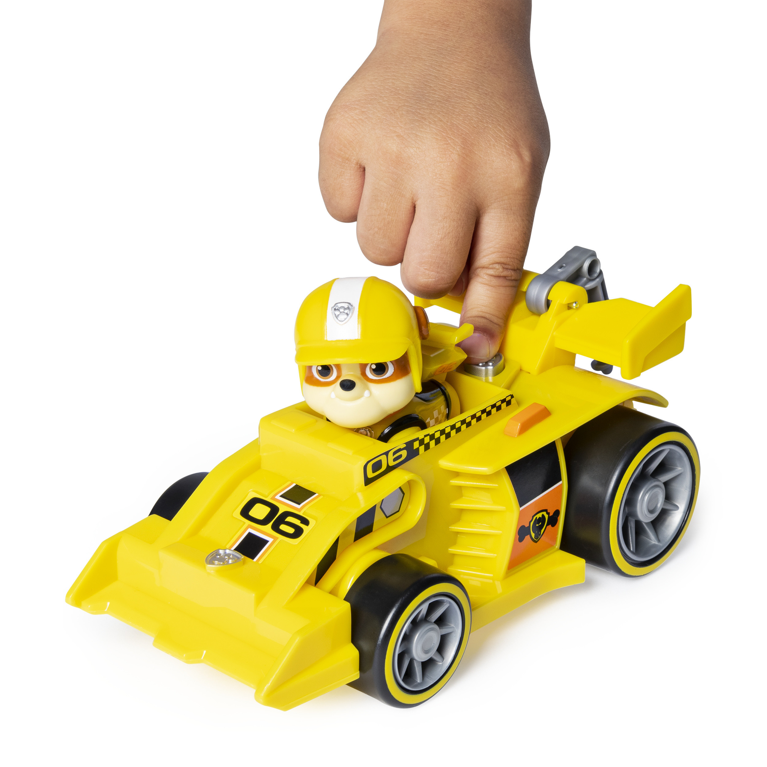 Een gele raceauto speelgoed met een hond in een helm, en een hand die op een knop drukt.