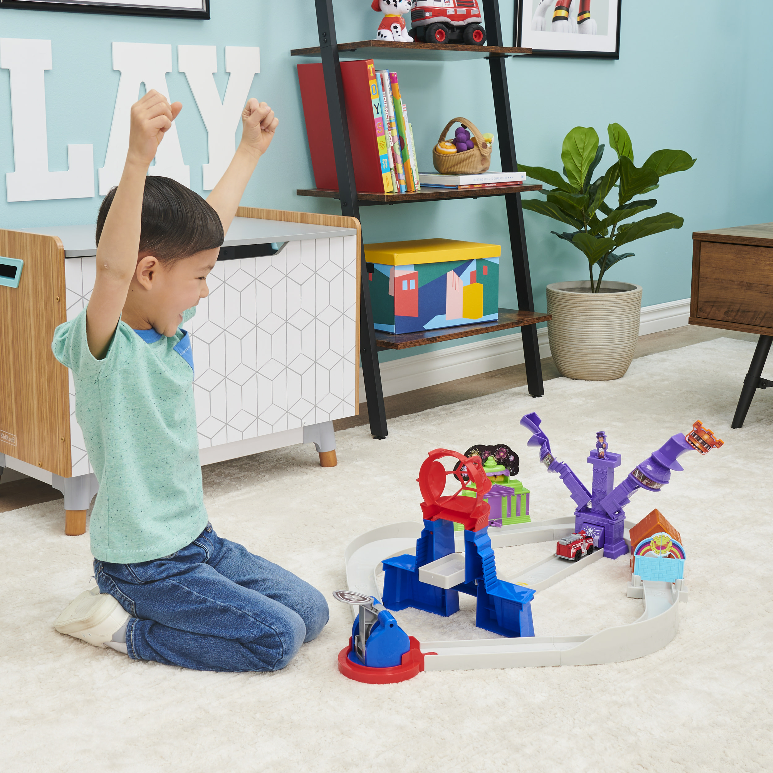 Chłopiec bawi się zabawką z torem, która zawiera zabawkę samochód i budynek.