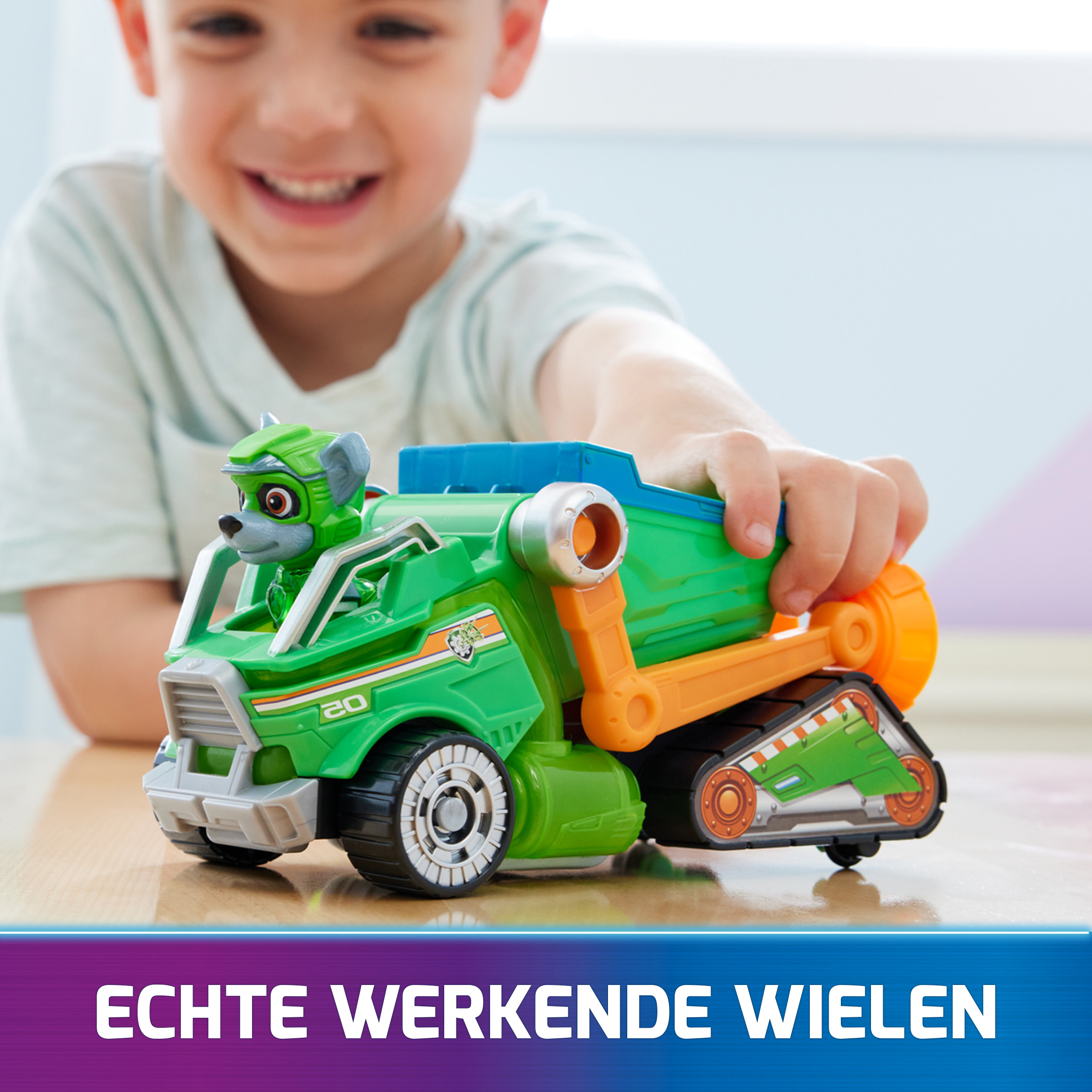 Ein Junge spielt mit einem grünen und orangenen Spielzeug-LKW mit Paw Patrol Figur.