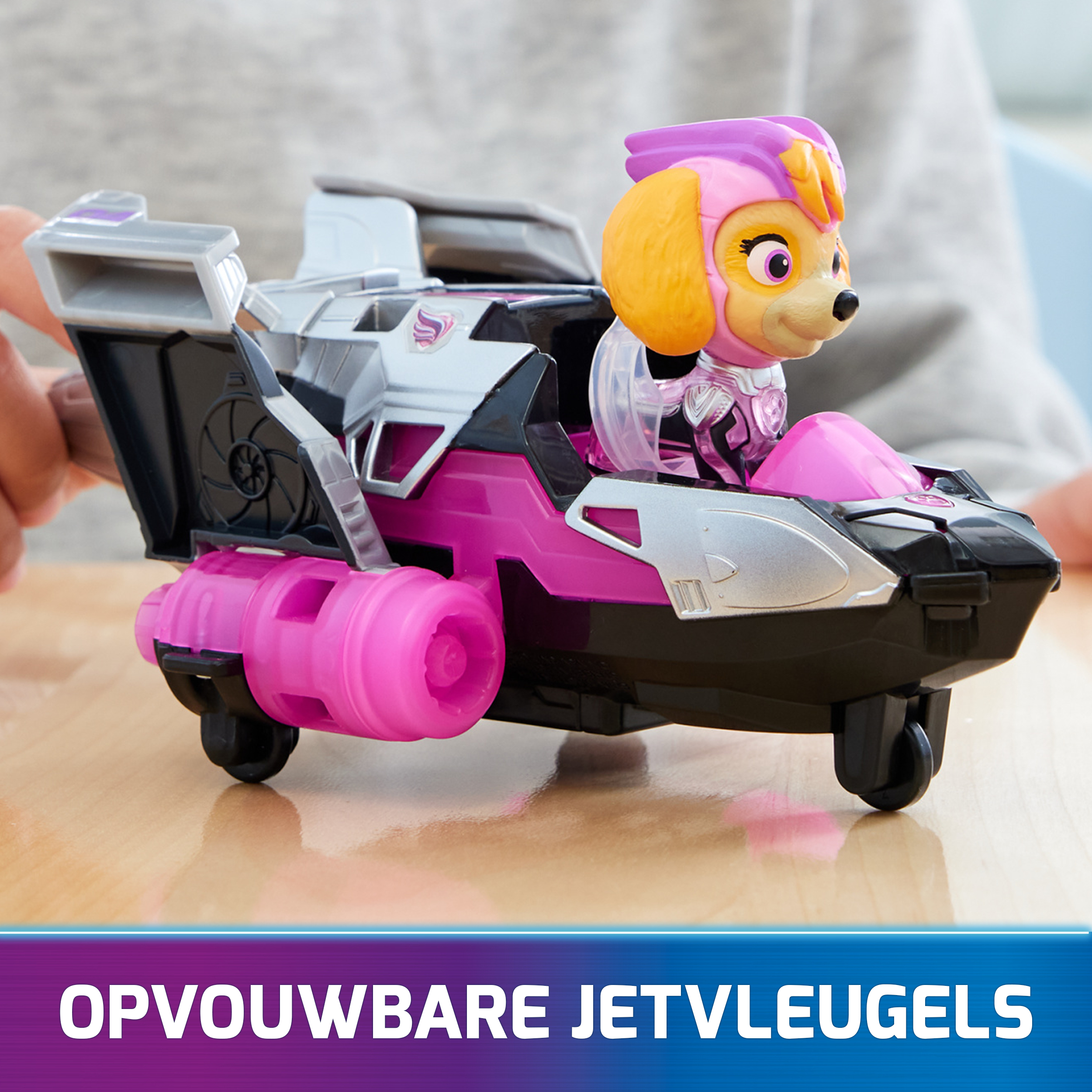 Skye z Psiego Patrolu w różowym i srebrnym odrzutowcu. Tekst: 'OPVOUWBARE JETVLEUGELS'.