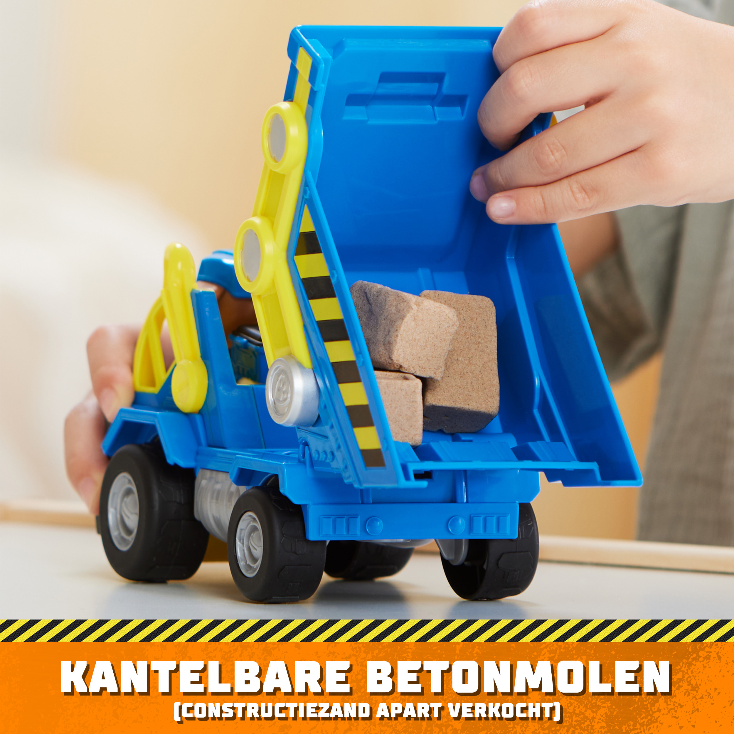 Ein blau-gelber Spielzeug-Muldenkipper, der von Kinderhänden gehalten wird und braune Blöcke transportiert.