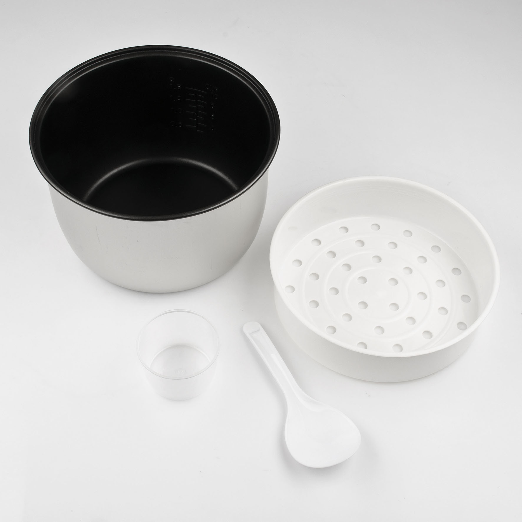 Ryżowar z wewnętrznym garnkiem, parowarem, miarką i łyżką na białym.