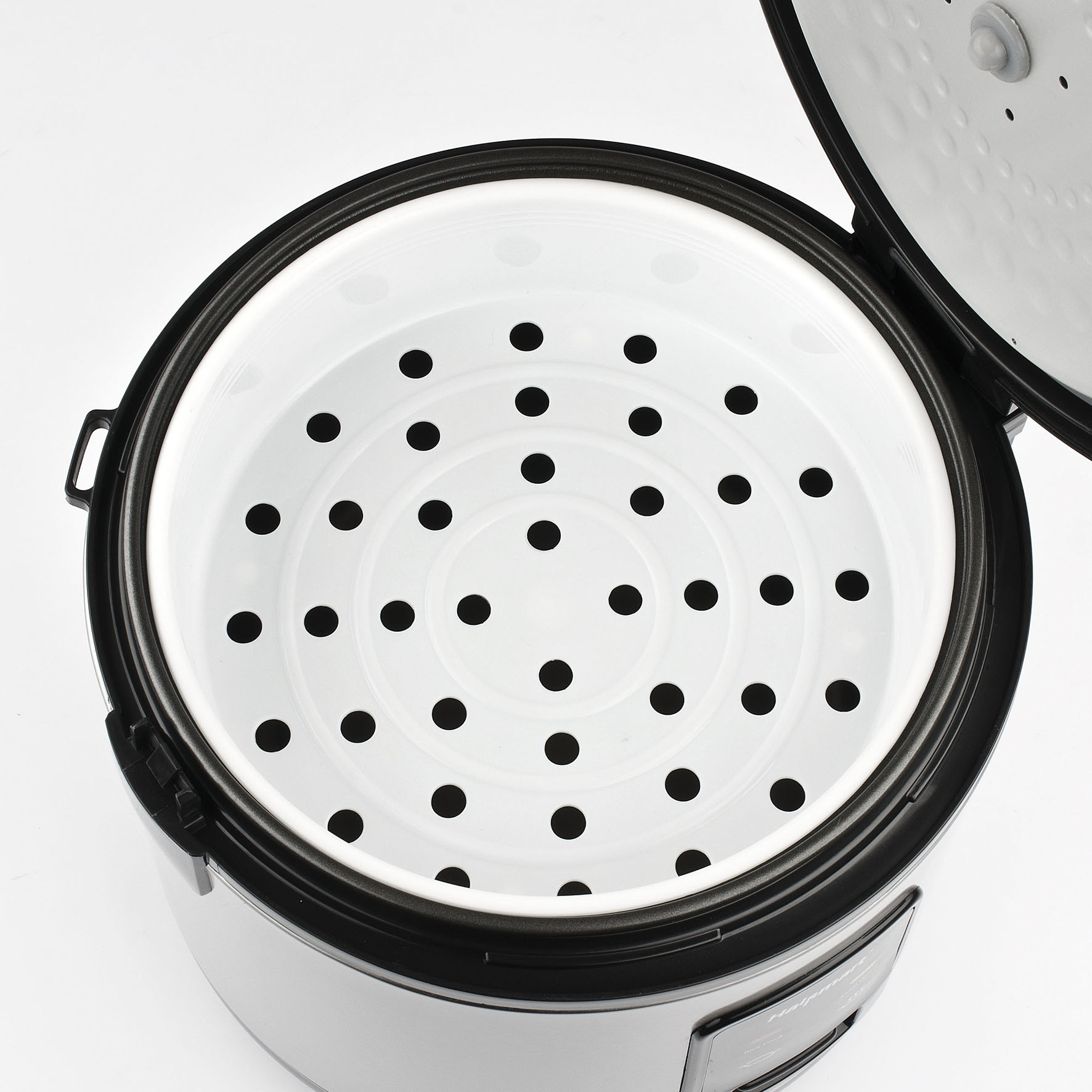 Wnętrze ryżowaru z białym garnkiem wewnętrznym i czarnym garnkiem zewnętrznym. W garnku są otwory.