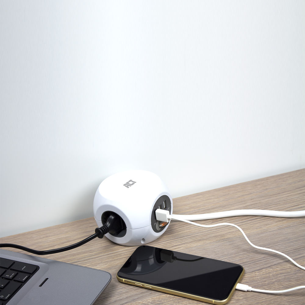 Biała kostka zasilająca na drewnianej powierzchni z podłączonym telefonem i laptopem.