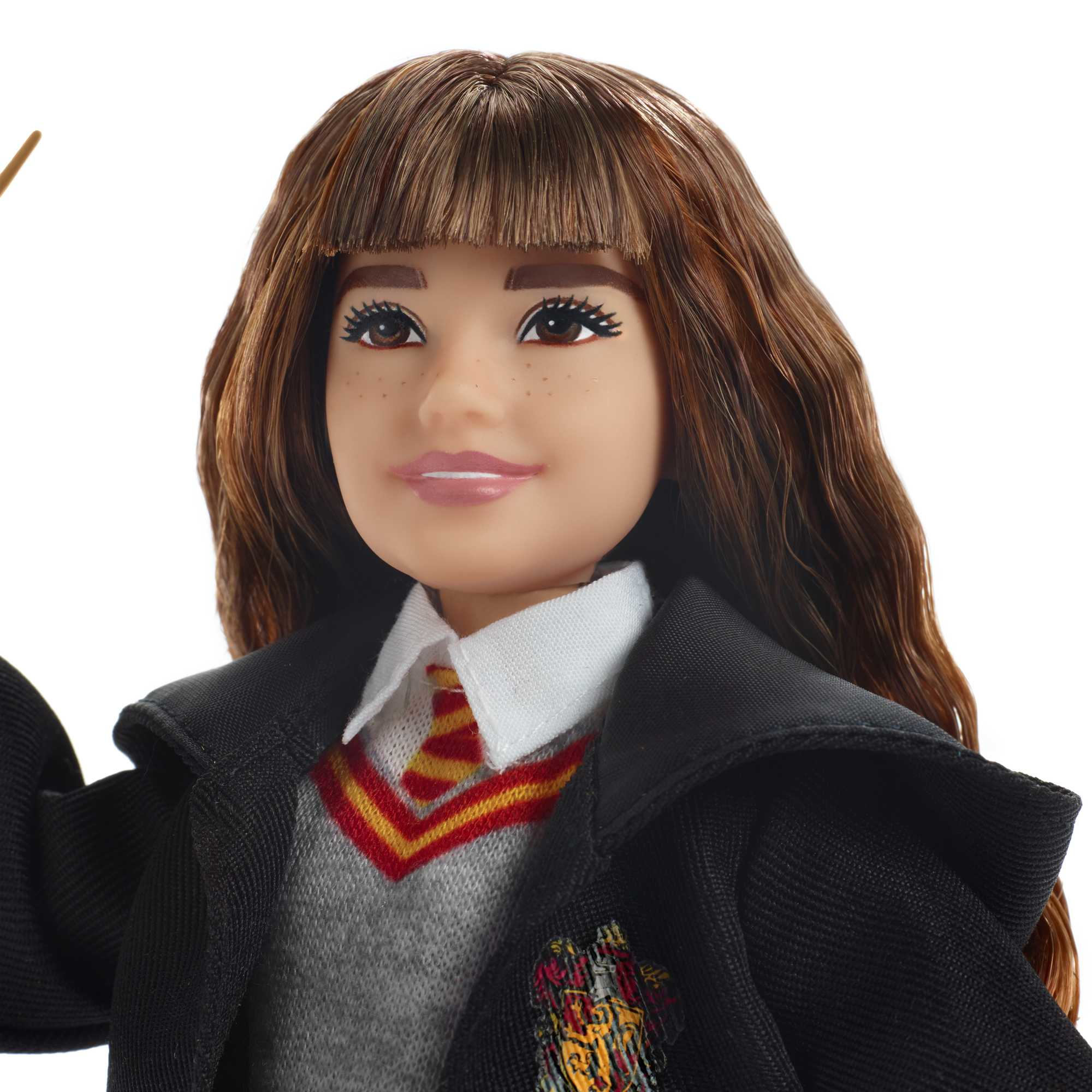 Nahaufnahme einer Hermione Granger-Puppe. Sie trägt eine Schuluniform mit Krawatte und einen schwarzen Umhang und hält einen Zauberstab.