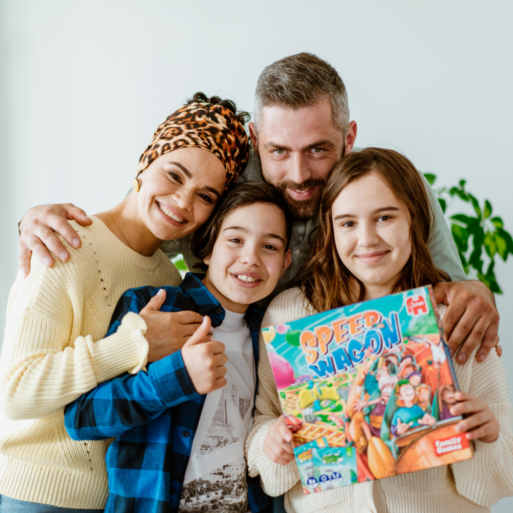 Familia de cuatro sonriendo, sosteniendo un juego de mesa. La madre lleva un pañuelo.