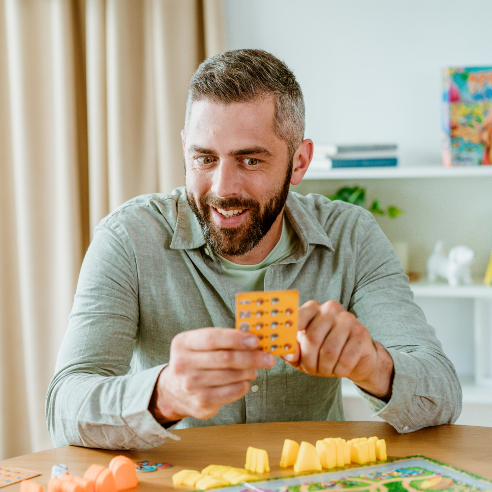 Hombre sosteniendo una tarjeta. Sonriendo, camisa. Habitación de fondo.