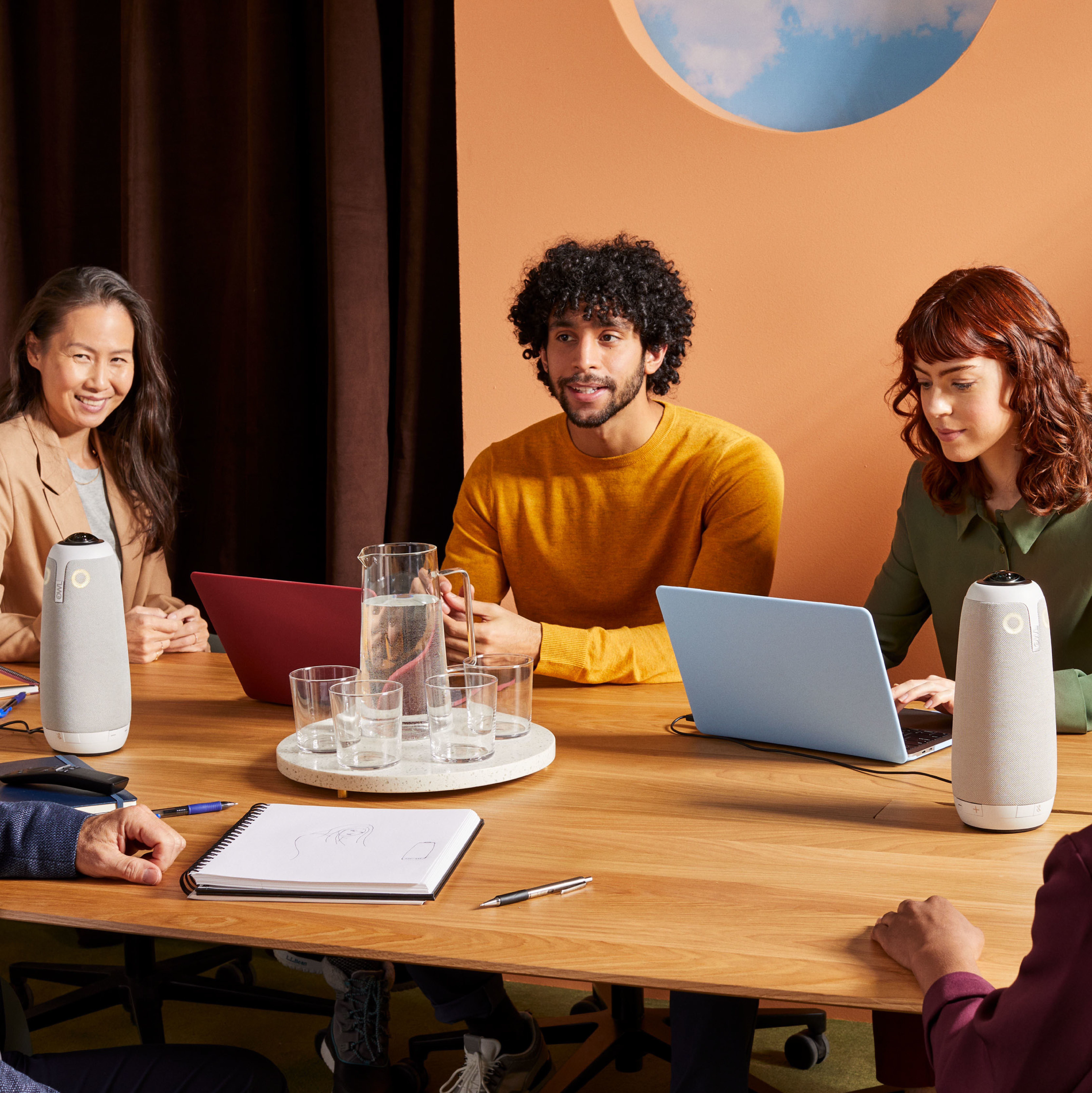 Besprechung mit 4 Personen an einem Tisch. Zwei Lautsprecher, Laptops und Wassergläser stehen auf dem Tisch.