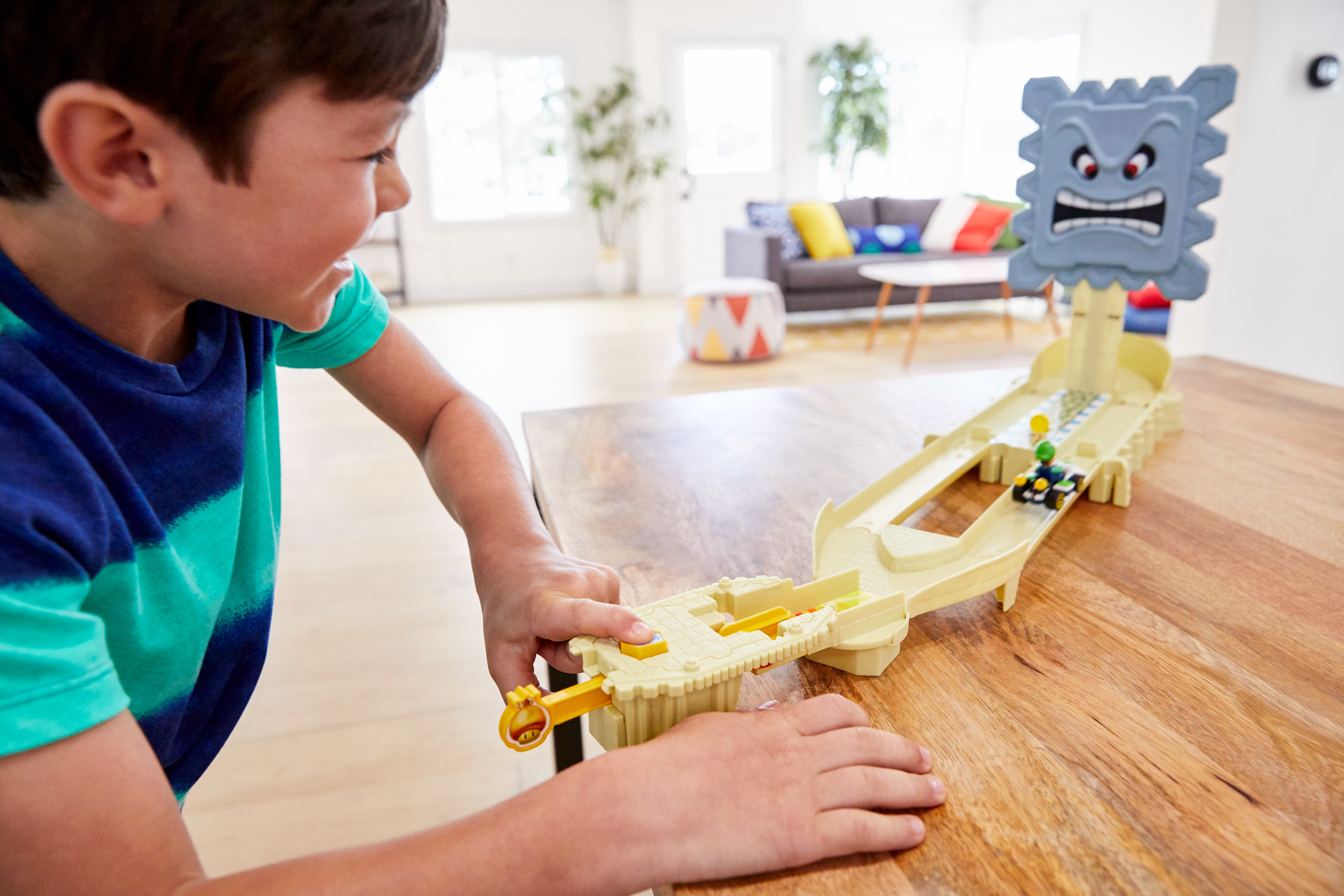 Ein Junge, der mit einer Mario Kart Spielzeugstrecke spielt. Eine Thwomp-Figur und Spielzeugautos sind sichtbar.