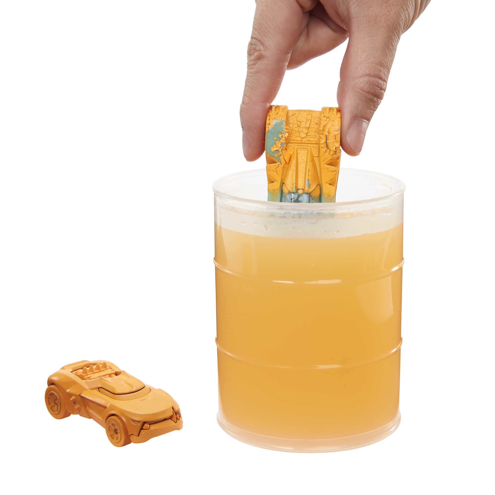 Ręka zanurza zabawkowy samochód w cieczy w przezroczystym pojemniku.