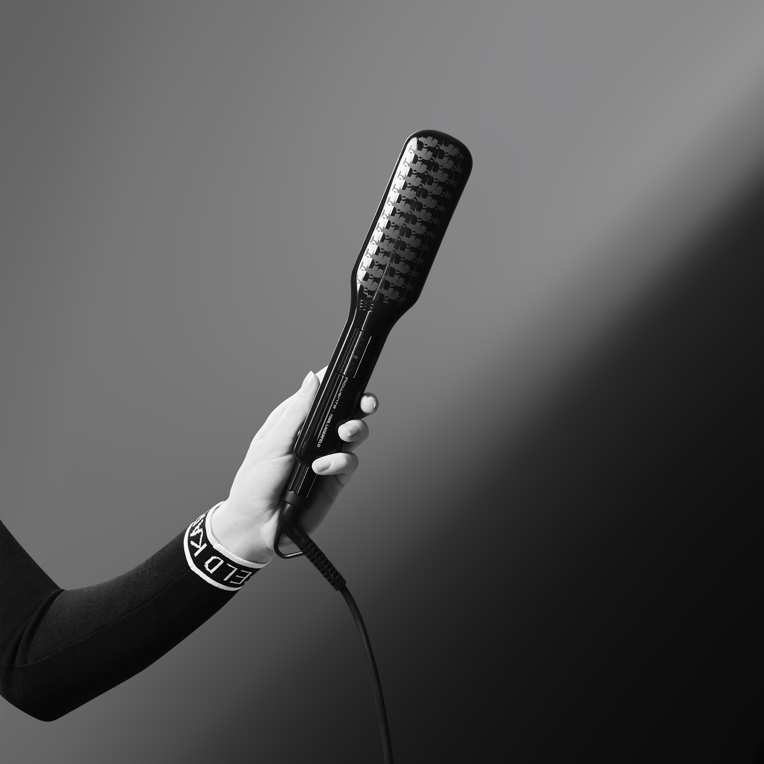 Dłoń kobiety trzymająca czarną szczotkę do prostowania włosów z czarno-białą bransoletką.