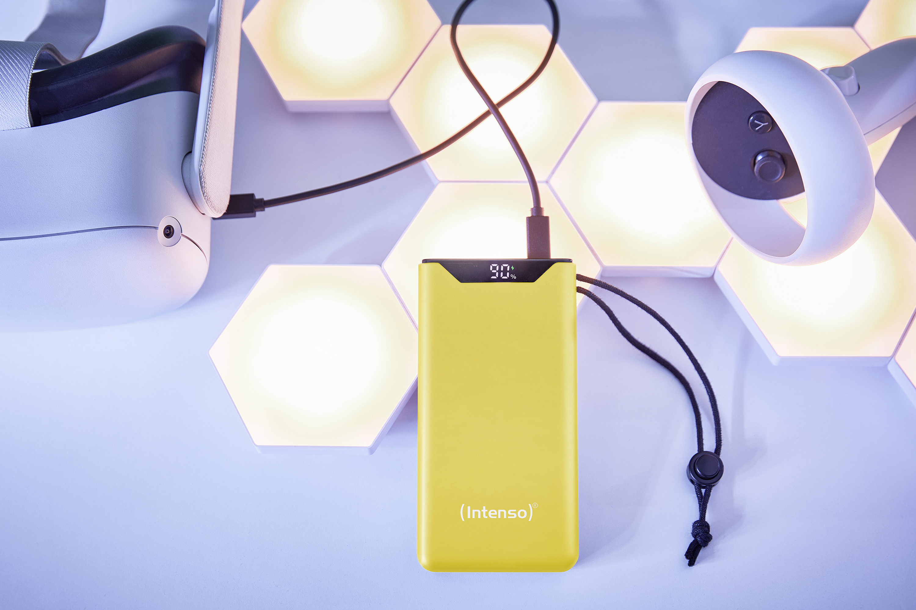 Batterie externe jaune avec affichage de charge à 90%. Casque VR et lumières en arrière-plan.