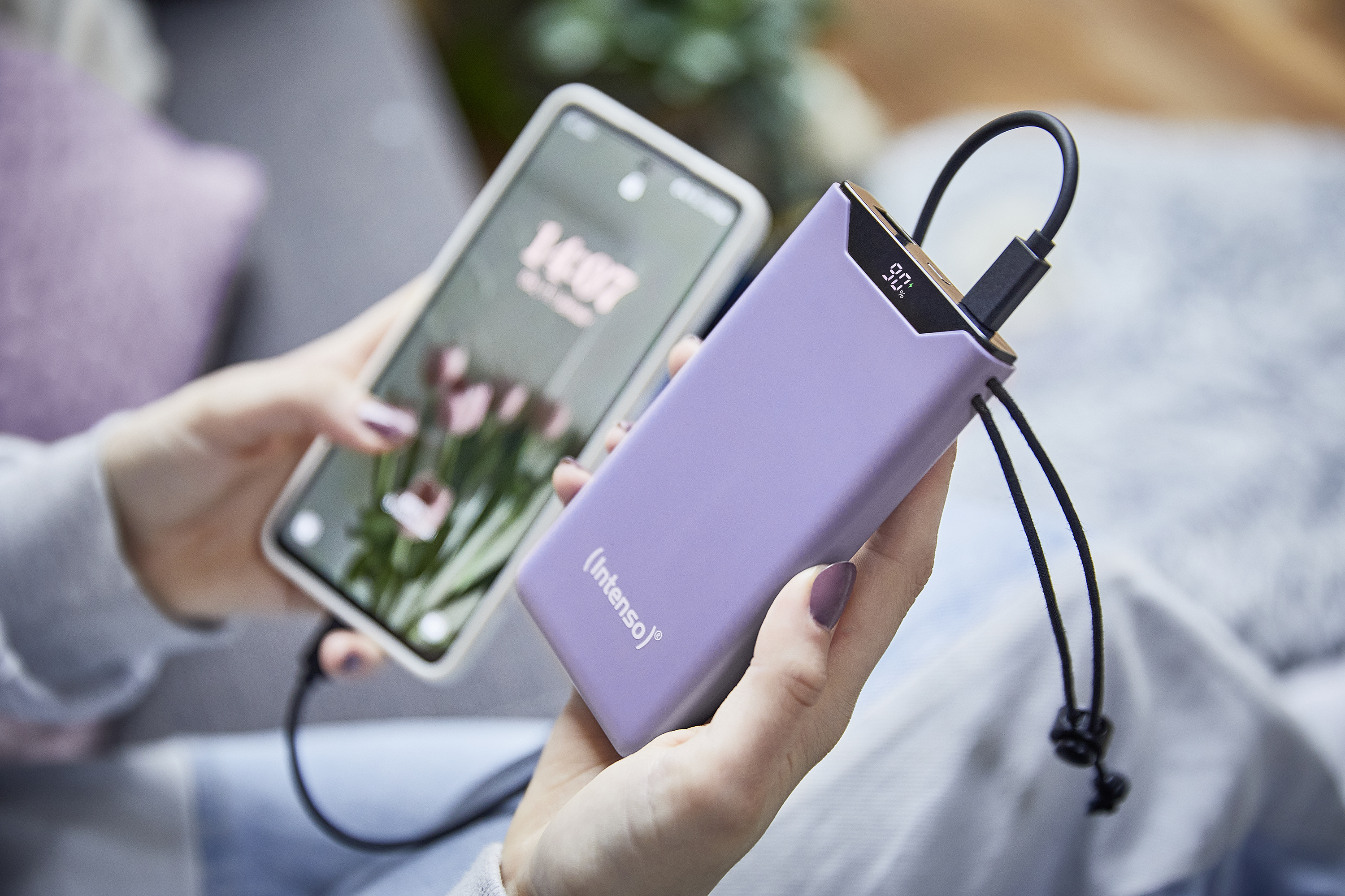 Vrouwenhanden die een paarse powerbank vasthouden die een telefoon oplaadt. De telefoon toont de tijd.