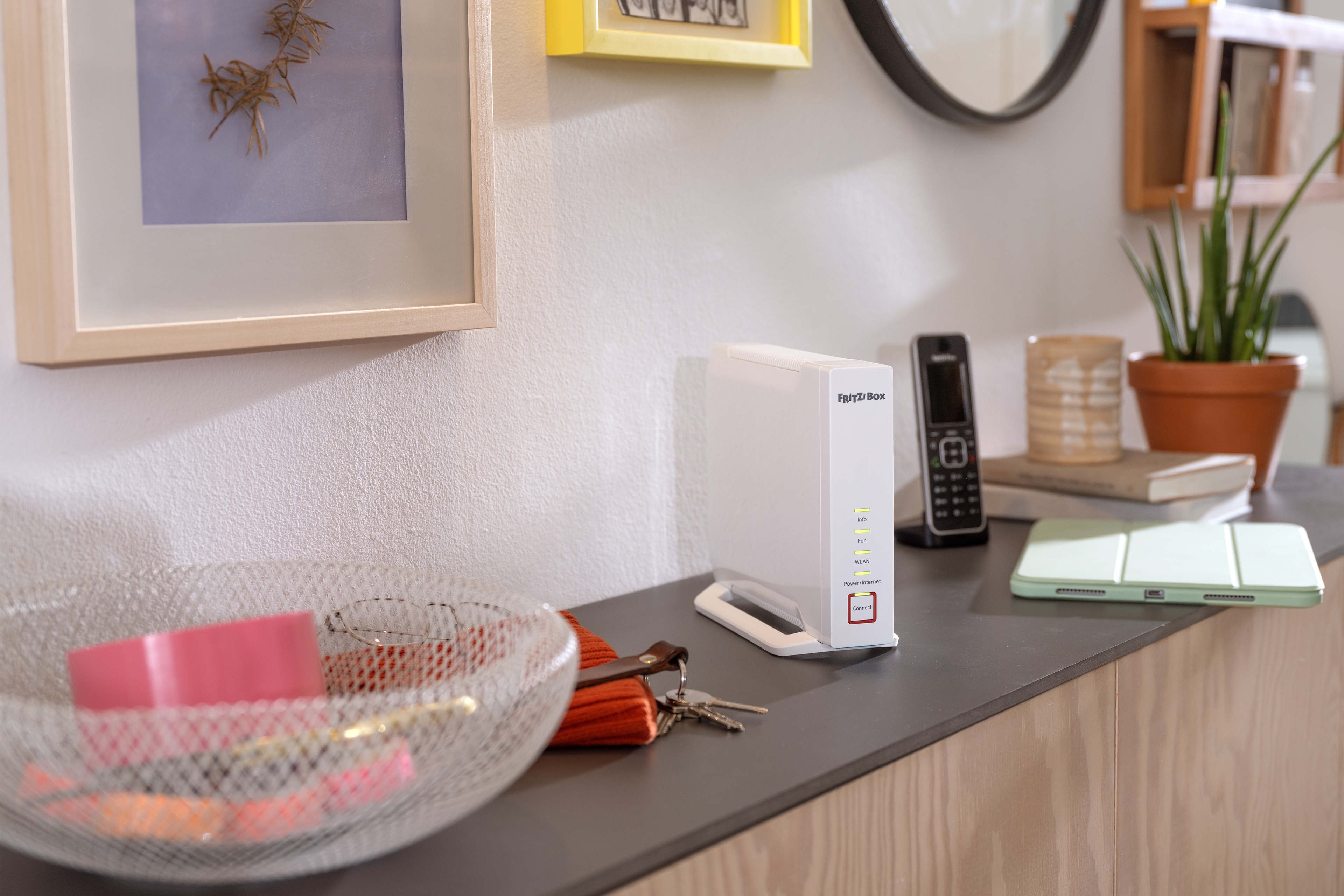 Routeur blanc sur une étagère avec décor. Téléphone, tablette et panier filaire avec objets roses sont visibles.