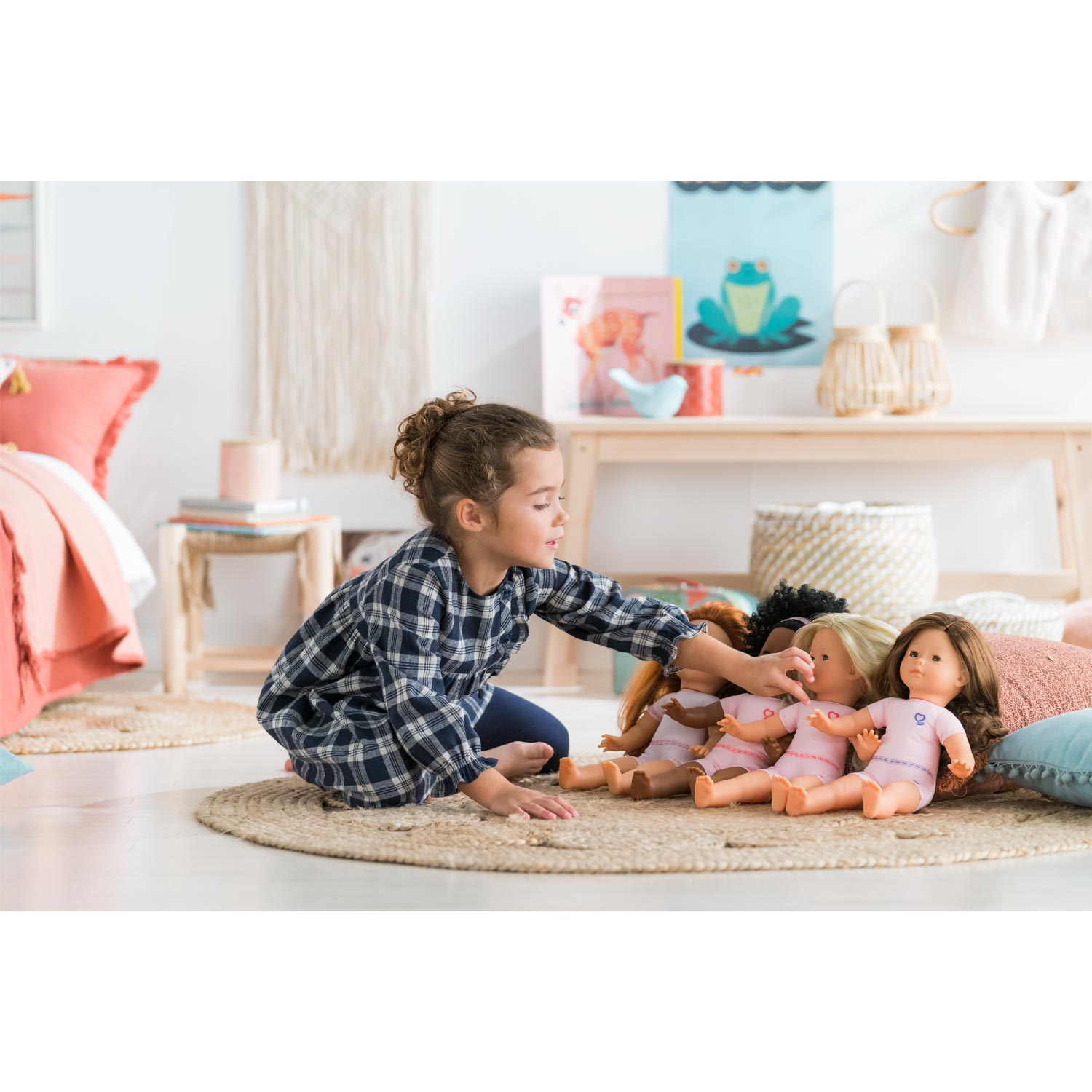 Dziewczynka sięga po lalki. Lalki są na dywanie, w tle półka.