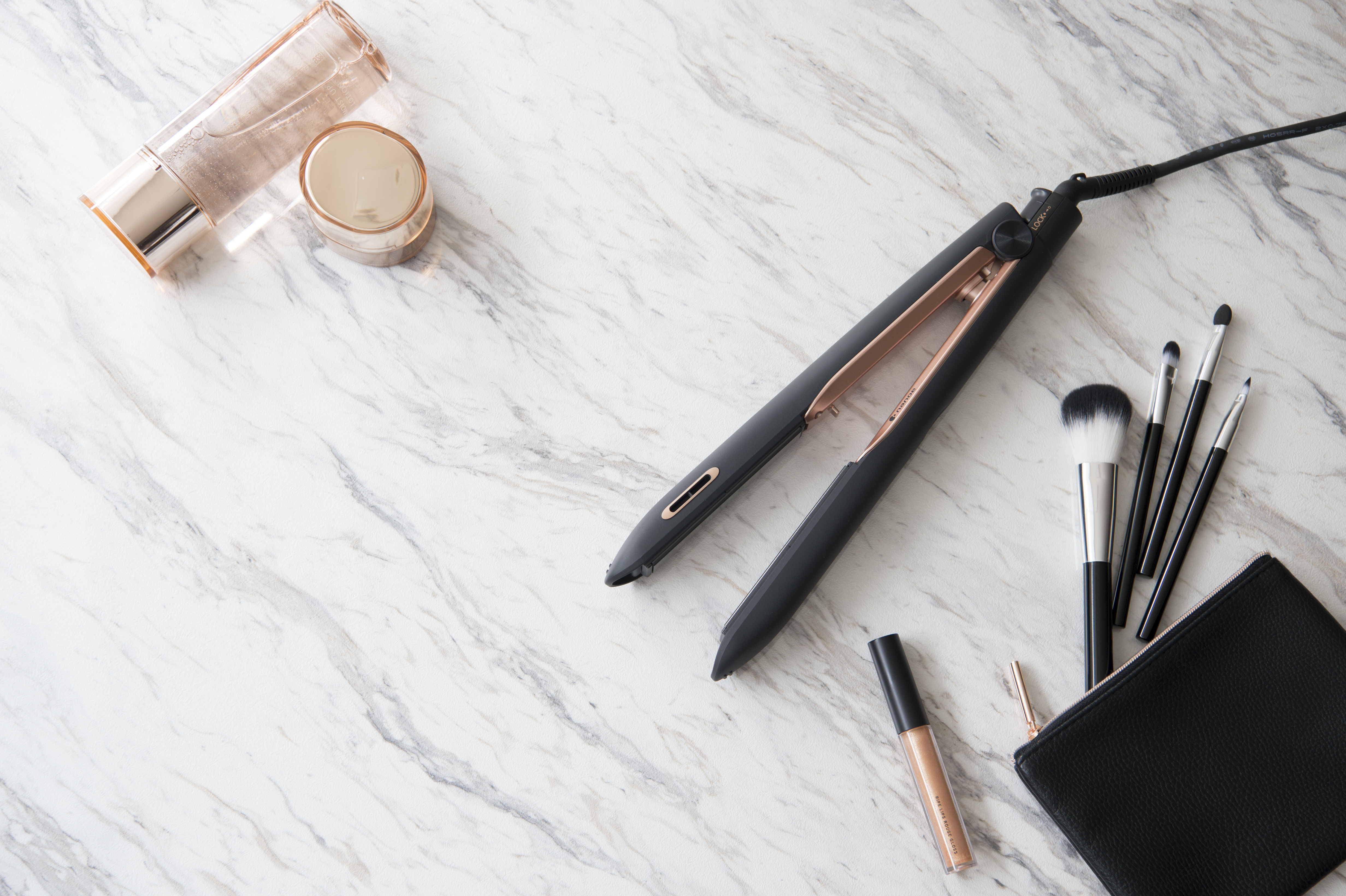 Plat gelegde beautyproducten en een stijltang op een marmeren oppervlak.