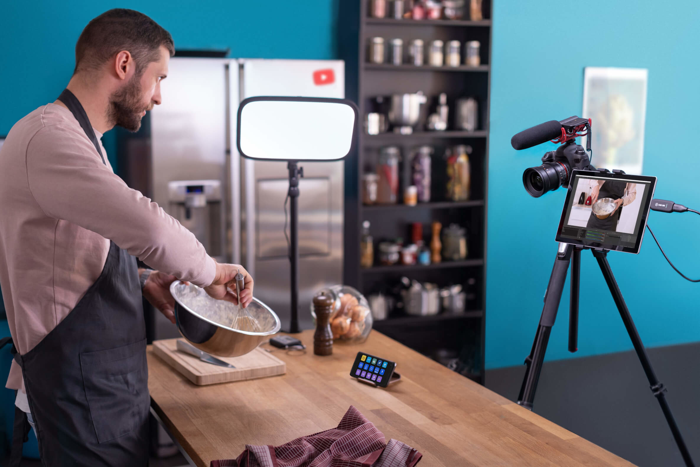 Mężczyzna gotuje w kuchni, używając tabletu do wideo. Kamera na statywie jest ustawiona do nagrywania.
