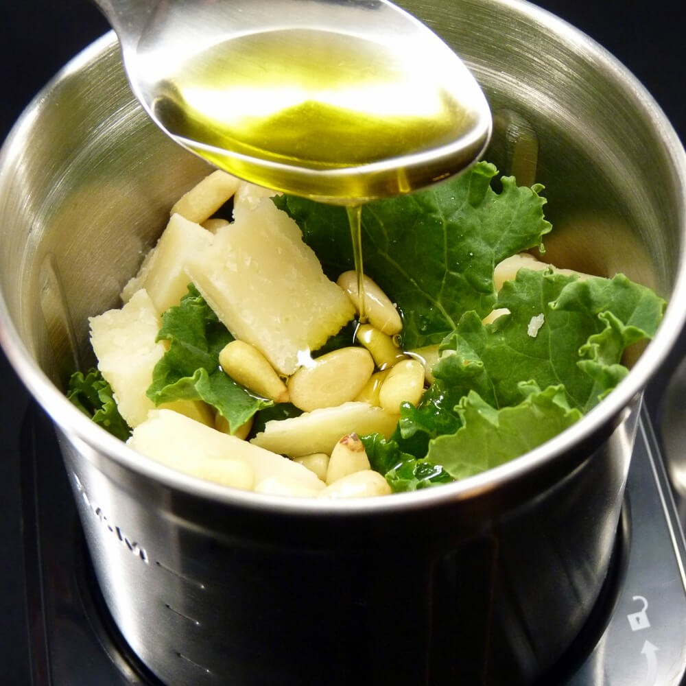 Oliwa z oliwek wlewana na składniki pesto, w tym ser, jarmuż i orzeszki piniowe.