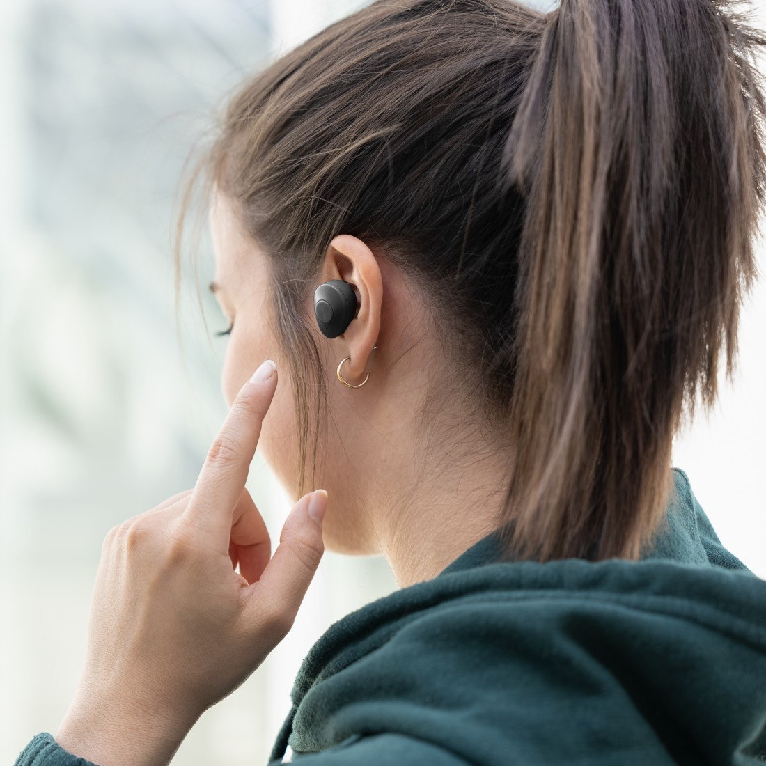 Kobieta w ciemnozielonej bluzie z kapturem, słuchająca muzyki za pomocą czarnych bezprzewodowych słuchawek.